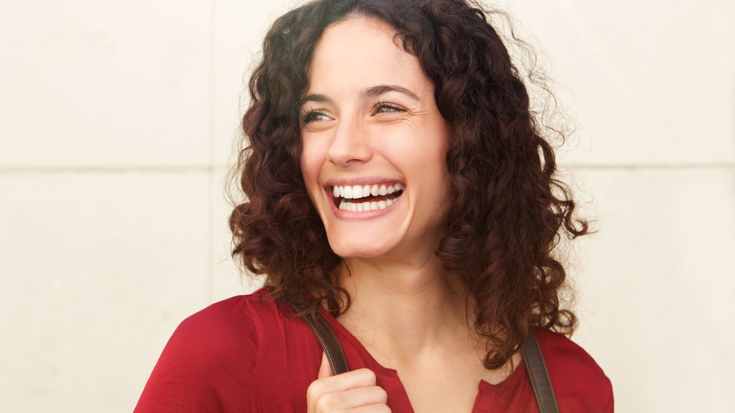Close up portrait of beautiful young woman laughing against white wall