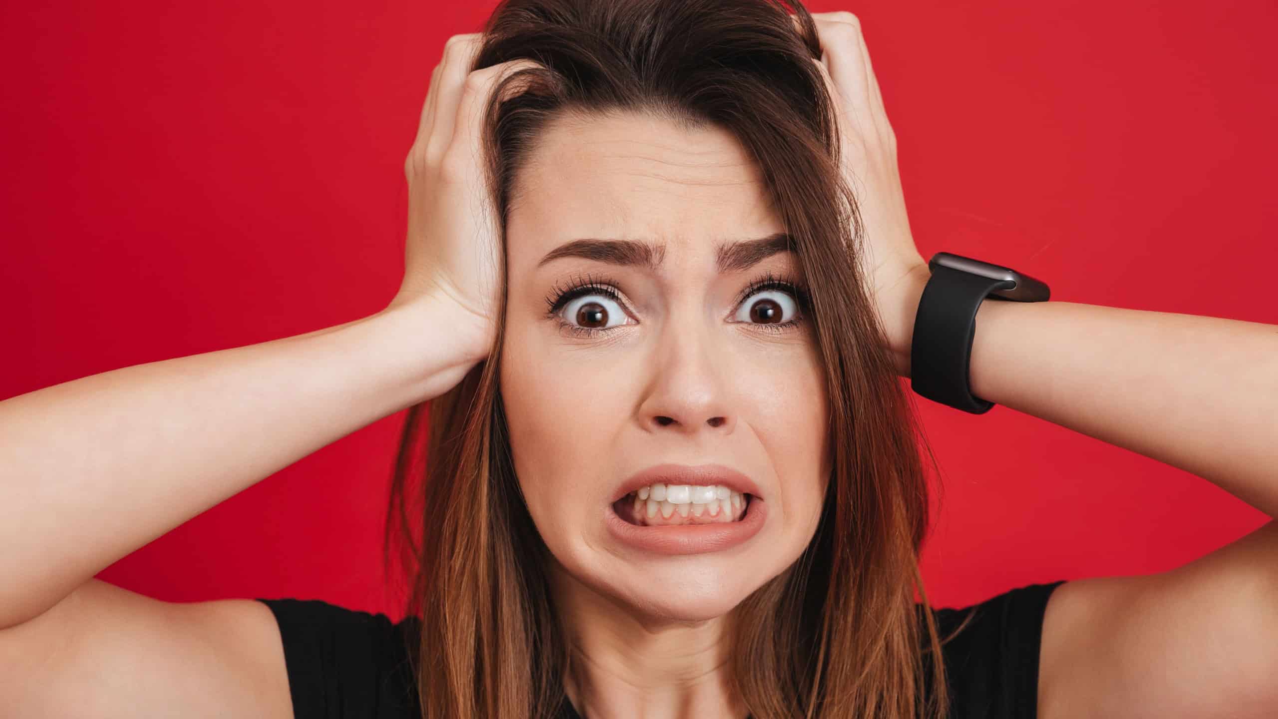 Portrait closeup of nervous woman grabbing her head and expressing problem or fright isolated over red background