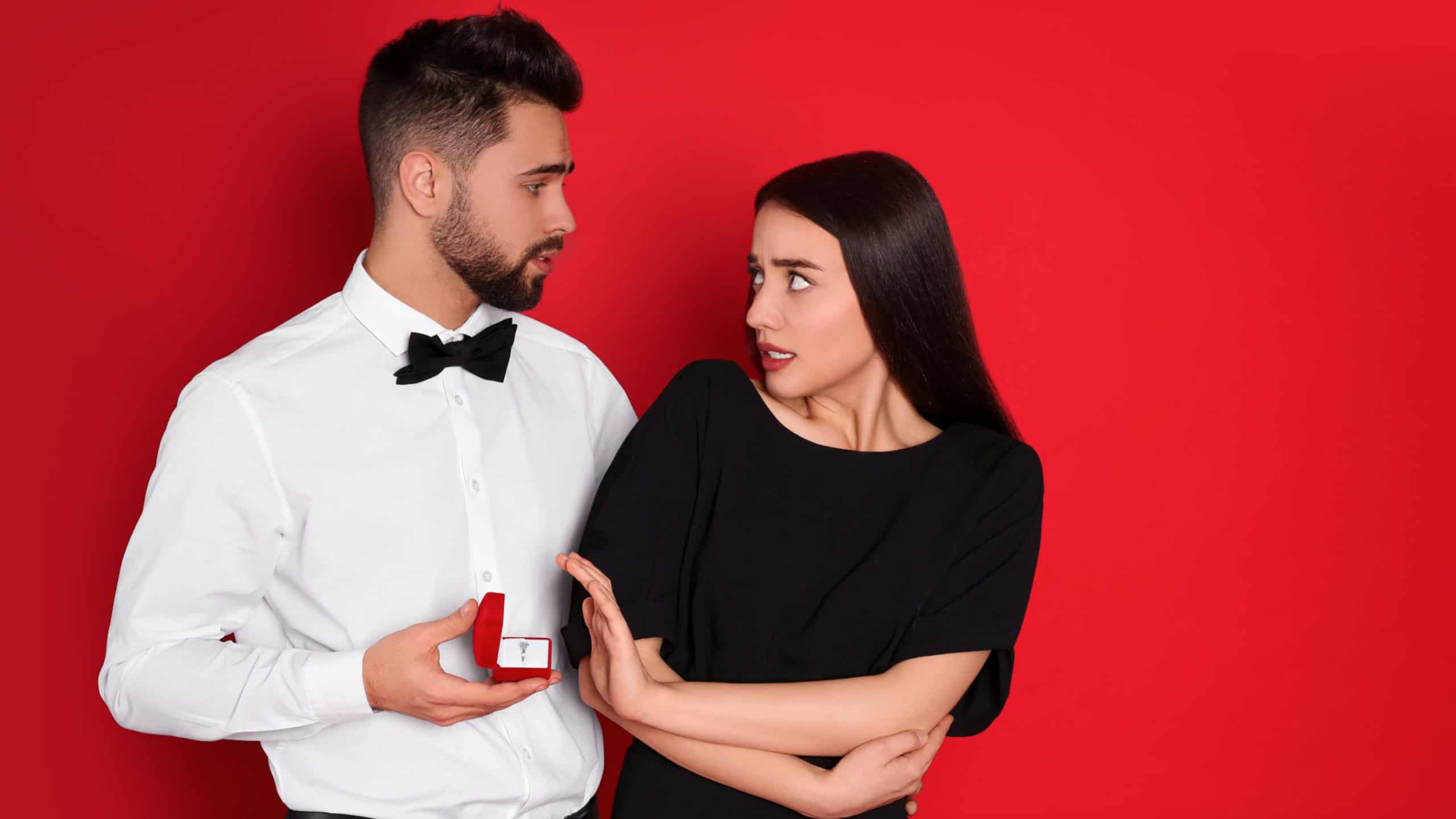 Young woman rejecting engagement ring from boyfriend on red background