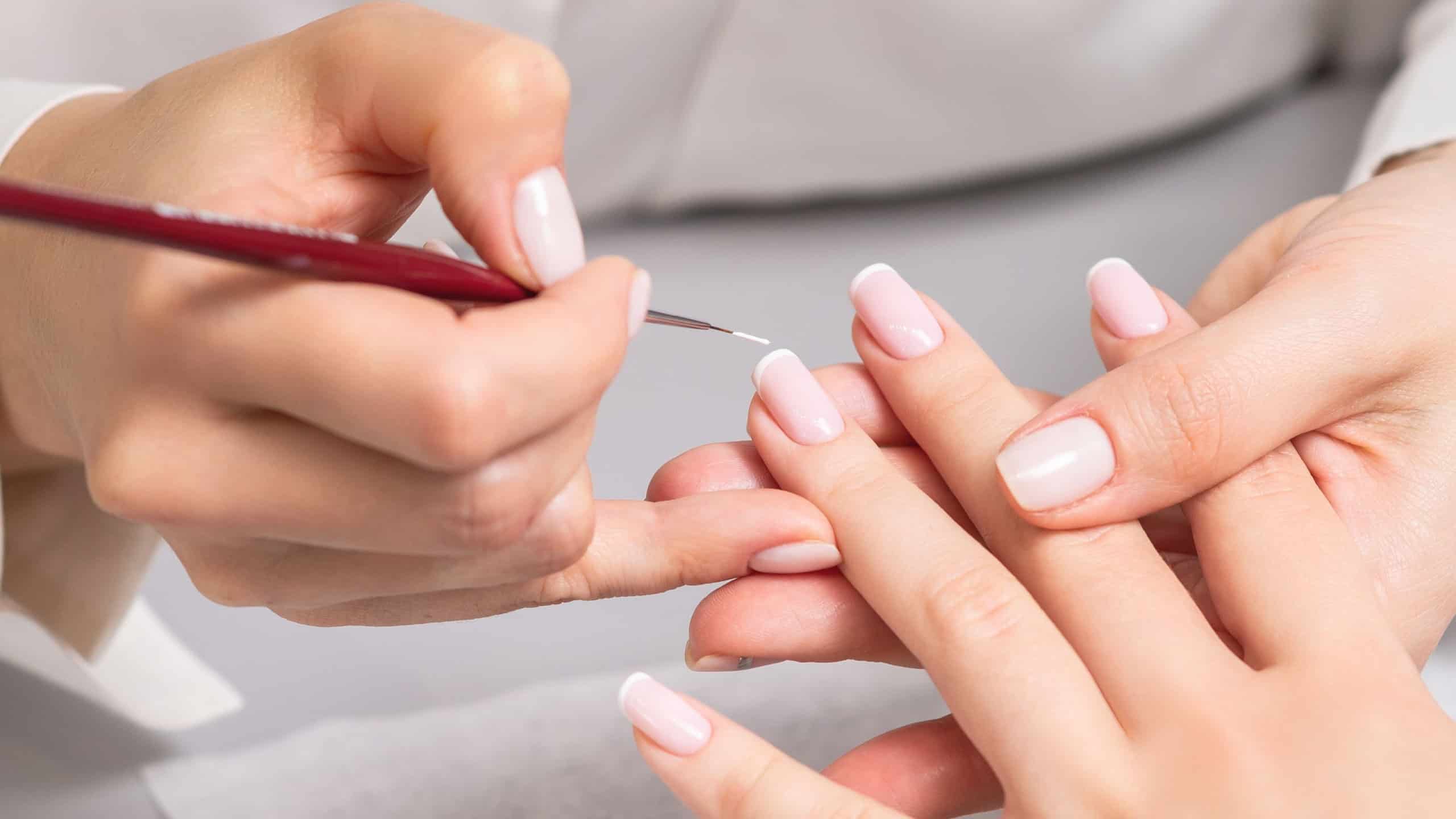Hand of young woman receiving french manicure by beautician at nail salon.