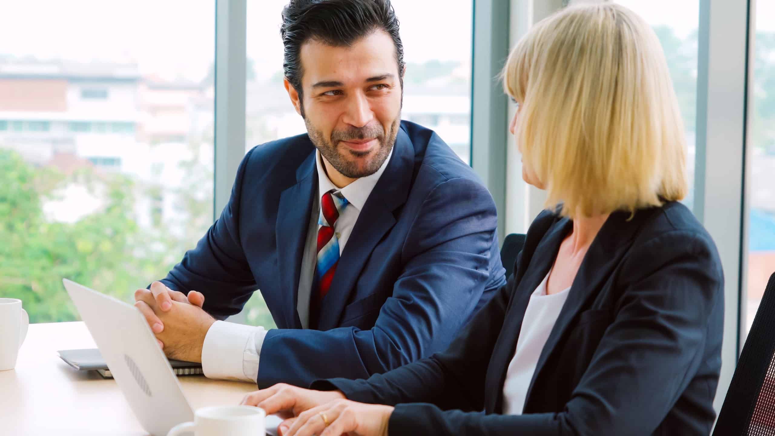Two business people talk project strategy at office meeting room. Businessman discuss project planning with colleague at modern workplace while having conversation and advice on financial data report.