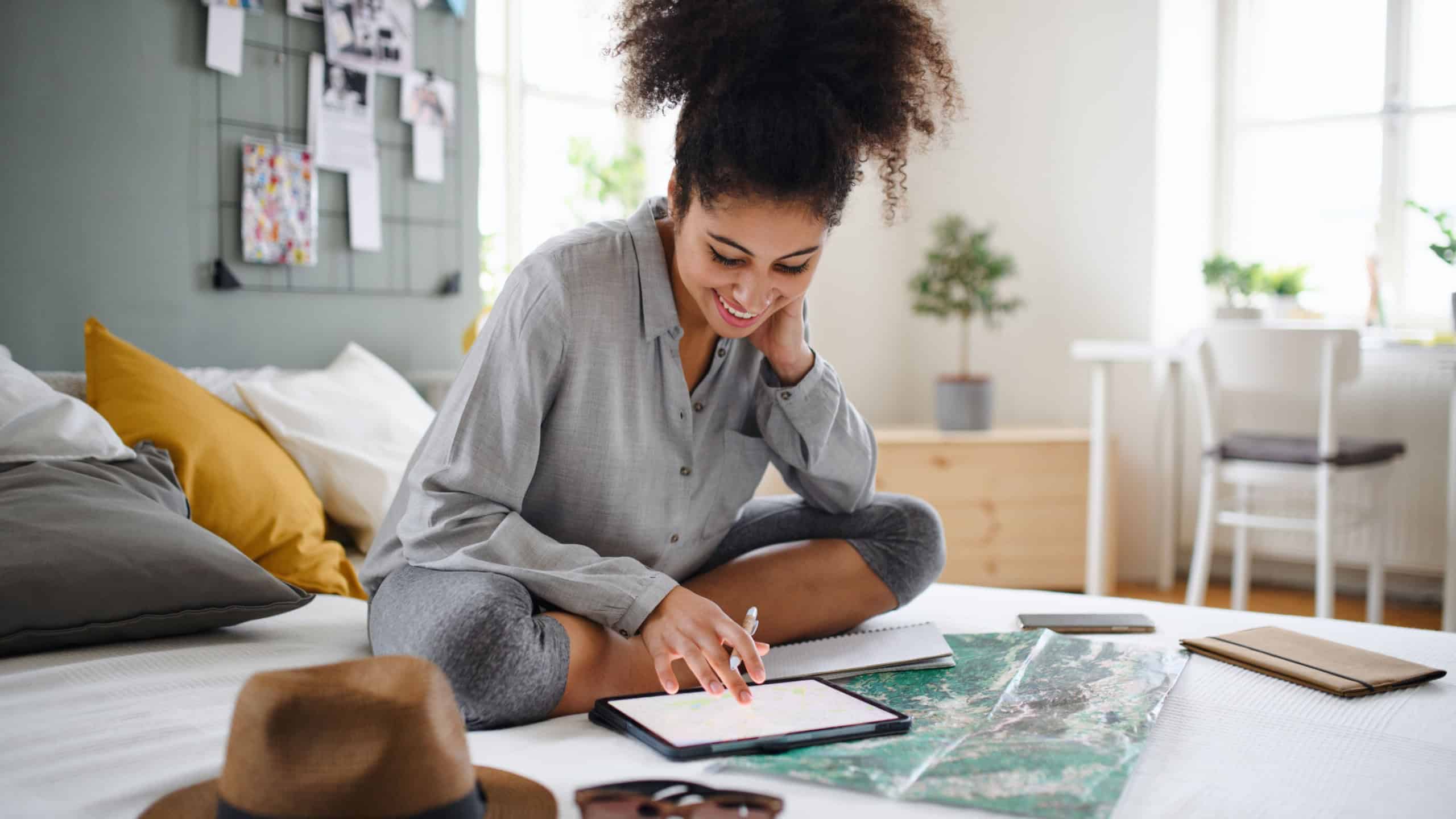 Young woman with tablet and map indoors at home, planning traveling trip.