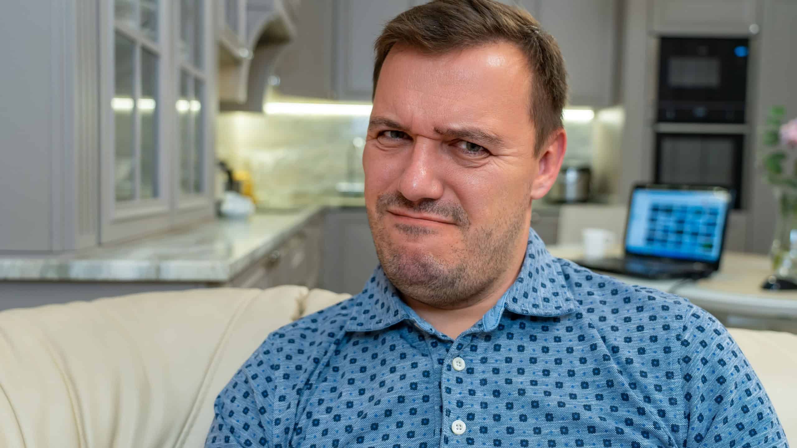 Annoyed millennial man with disgust look at camera at modern living room. Portrait of manager cringe and looking with squeamishness, bad joke or inappropriate content.