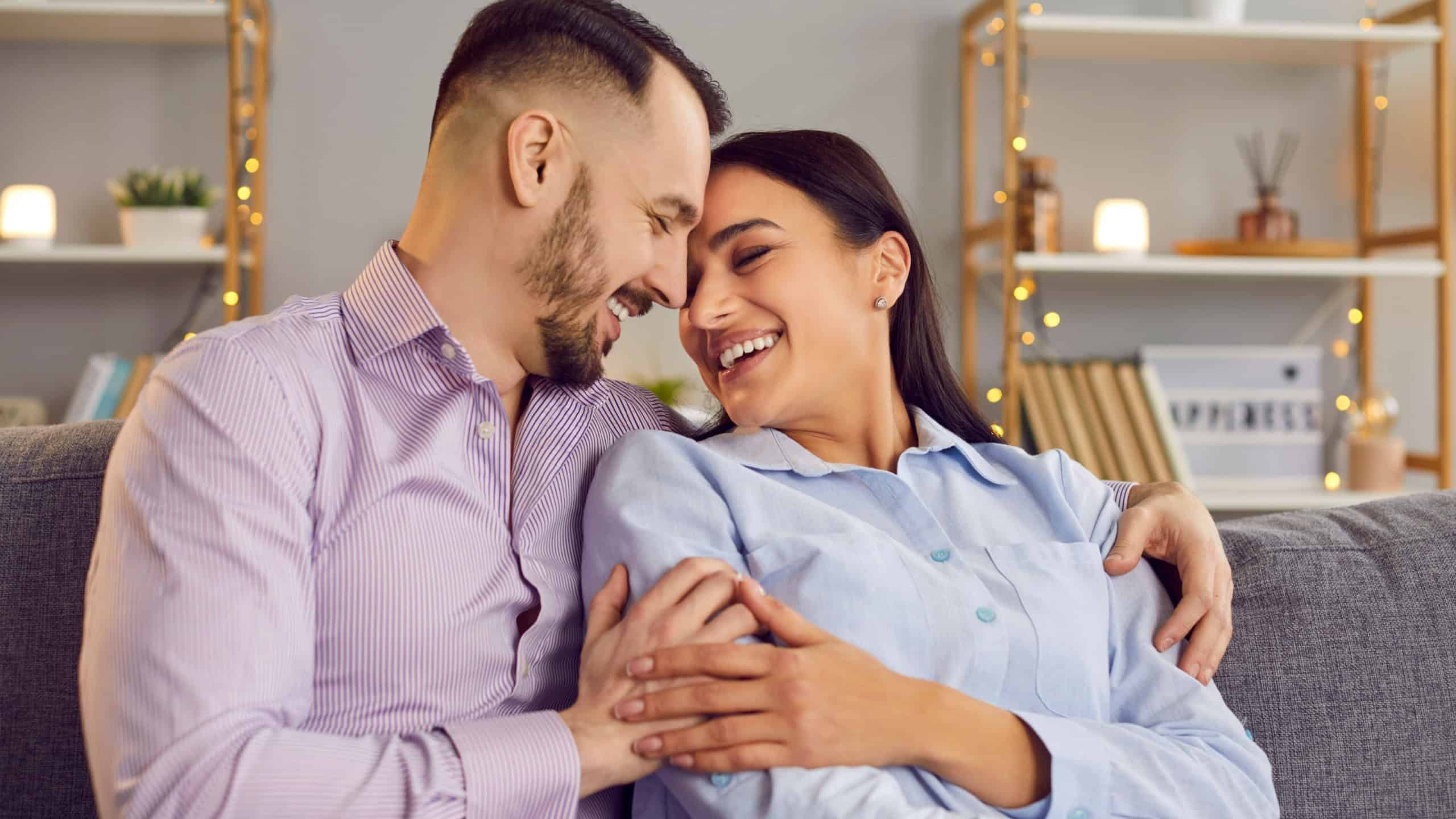 Happy and loving family couple shares a warm embrace on the sofa in the comfort of home. Smiles radiate happiness, capturing a beautiful moment of love, togetherness, and domestic bliss.