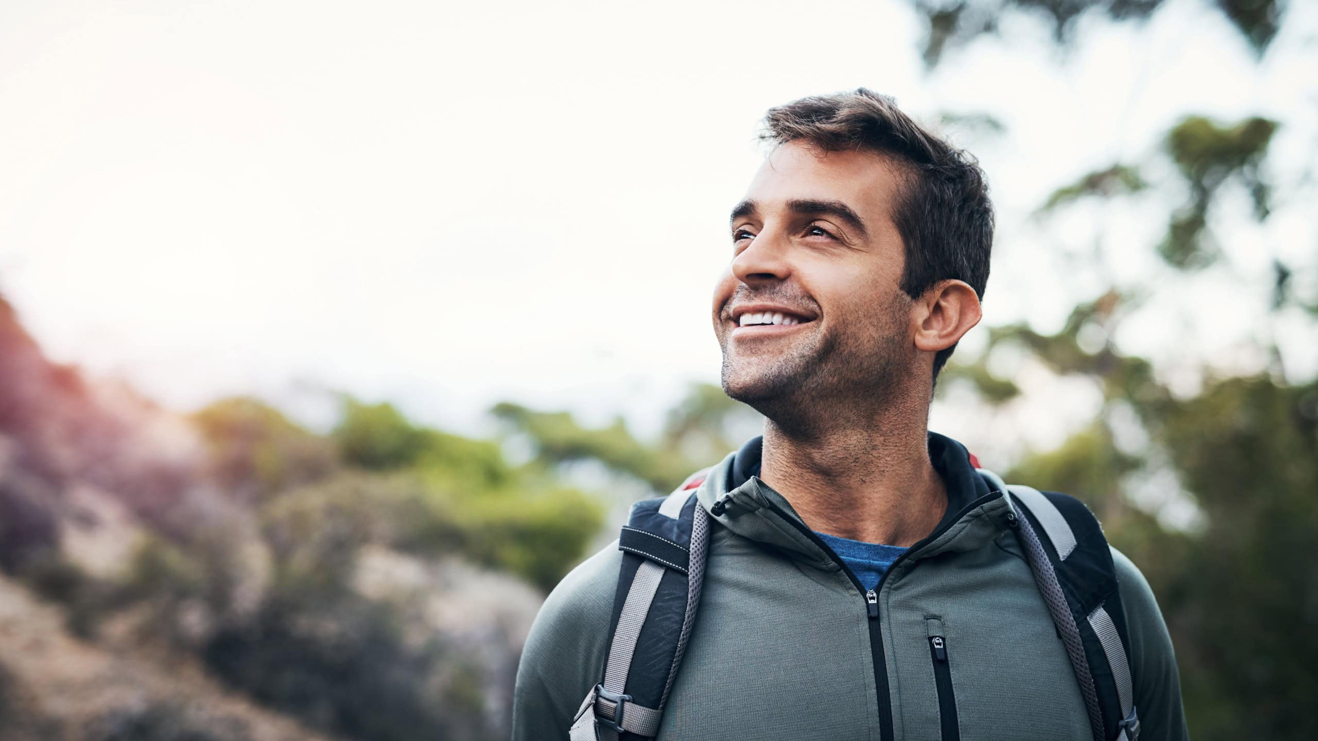 Man, backpack and hiking in outdoor forest for wilderness experience, exploration and solitude for stress relief or mental health. Guy, nature and happy in woods for adventure or physical exercise.