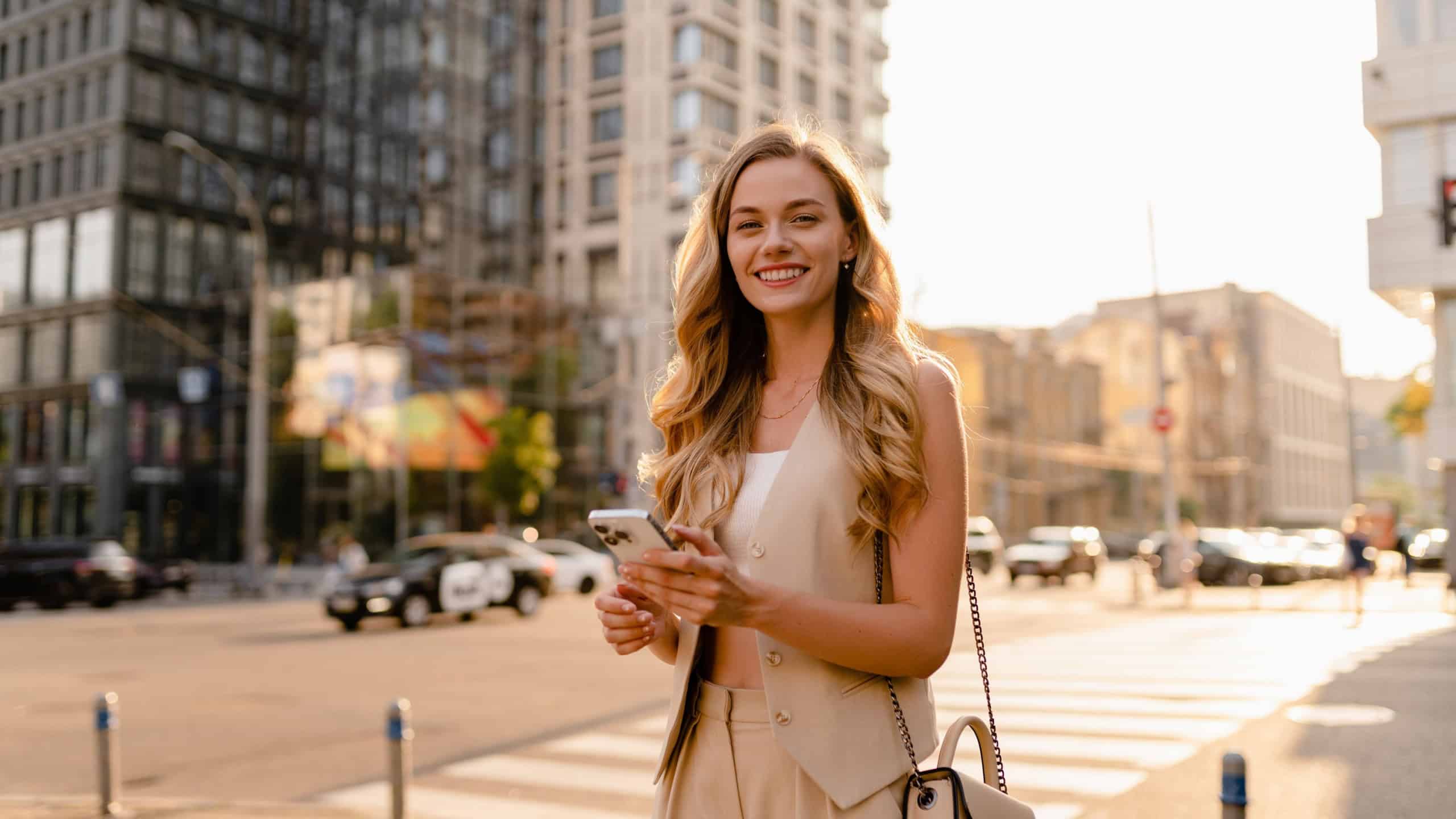 pretty blonde woman walking in sunny city street with phone, urban fashion style, smiling, summer trend season, business lady, using smartphone