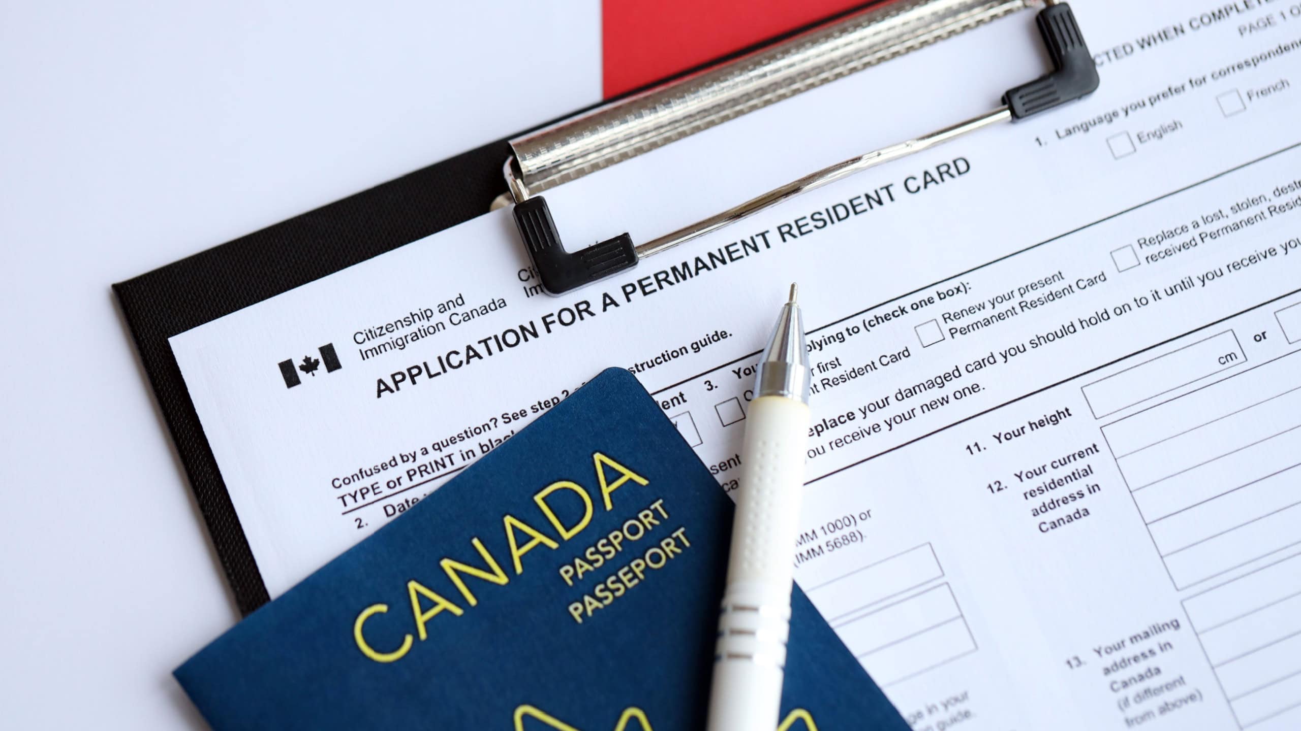 Application for permanent resident card on table with pen and canadian passport close up