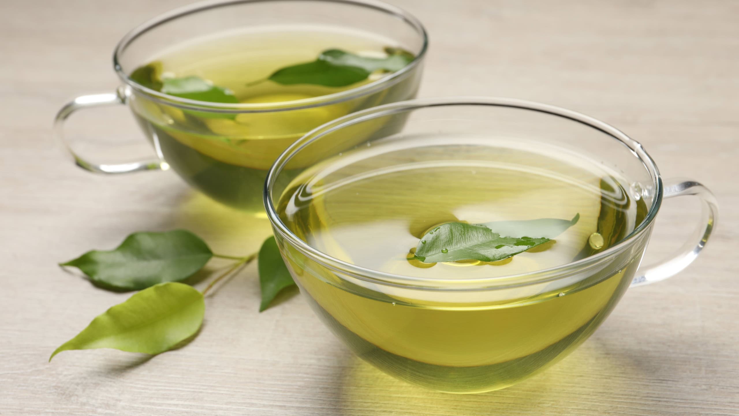 Refreshing green tea in cups and leaves on wooden table, closeup