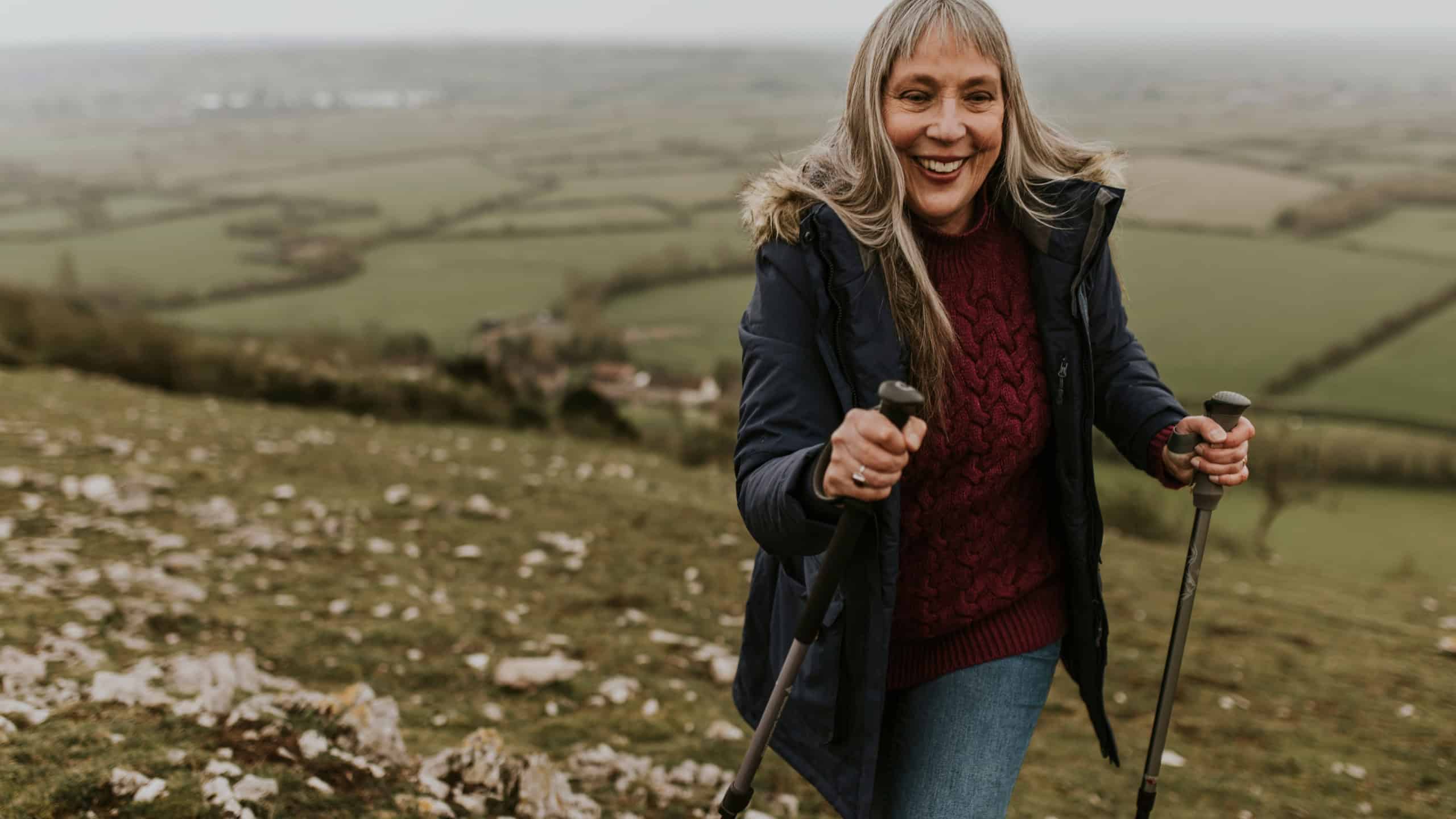 Senior woman hiking mountain, countryside, outdoor travel. Senior woman walking in nature. Health and wellness for senior retired woman. Woman enjoying a walk in the countryside nature.