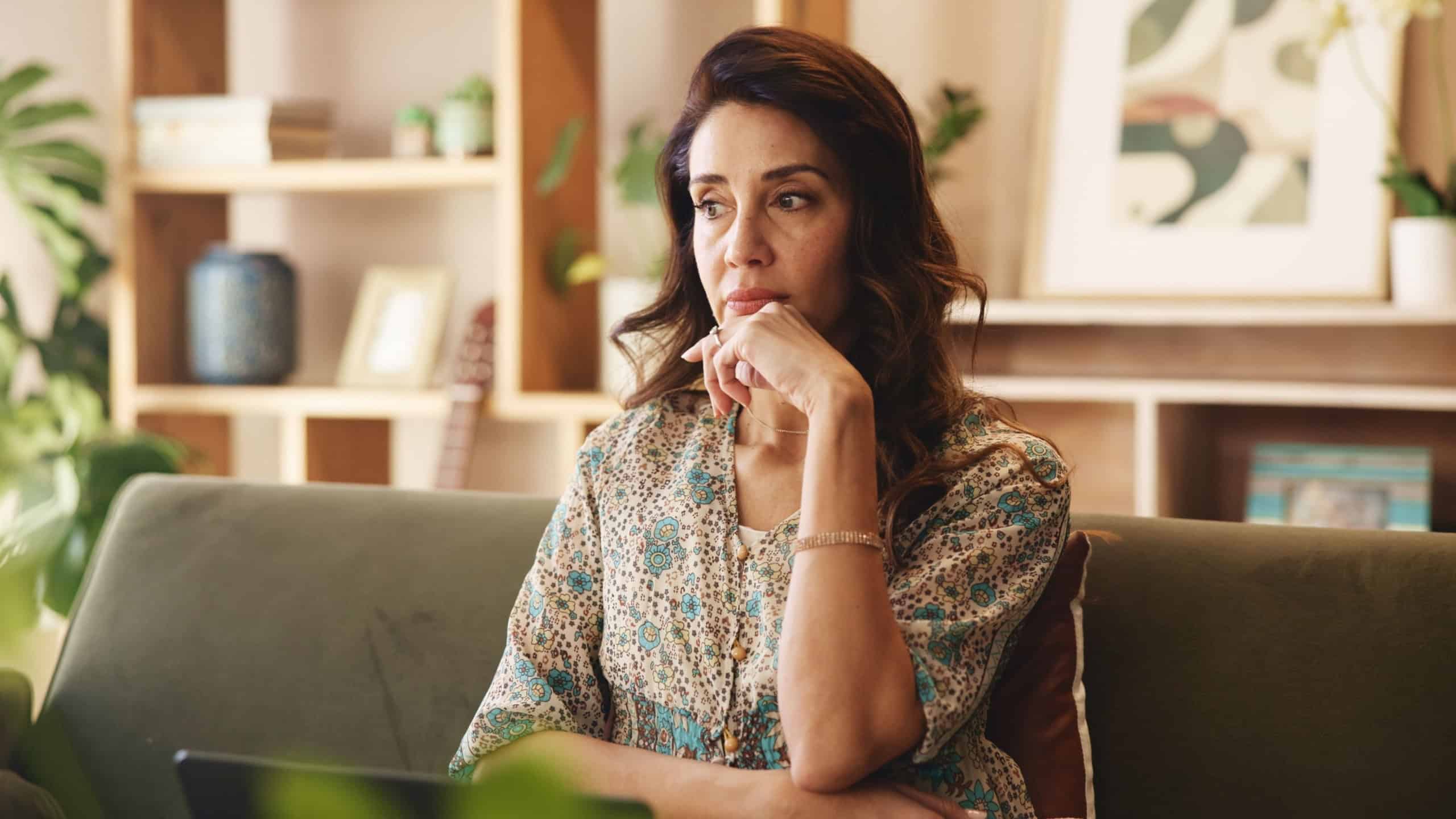 Mature, woman and thinking on sofa with stress in home for financial crisis, recession news and worried. Person, thoughtful and reflection on couch in lounge with debt anxiety and depression in house