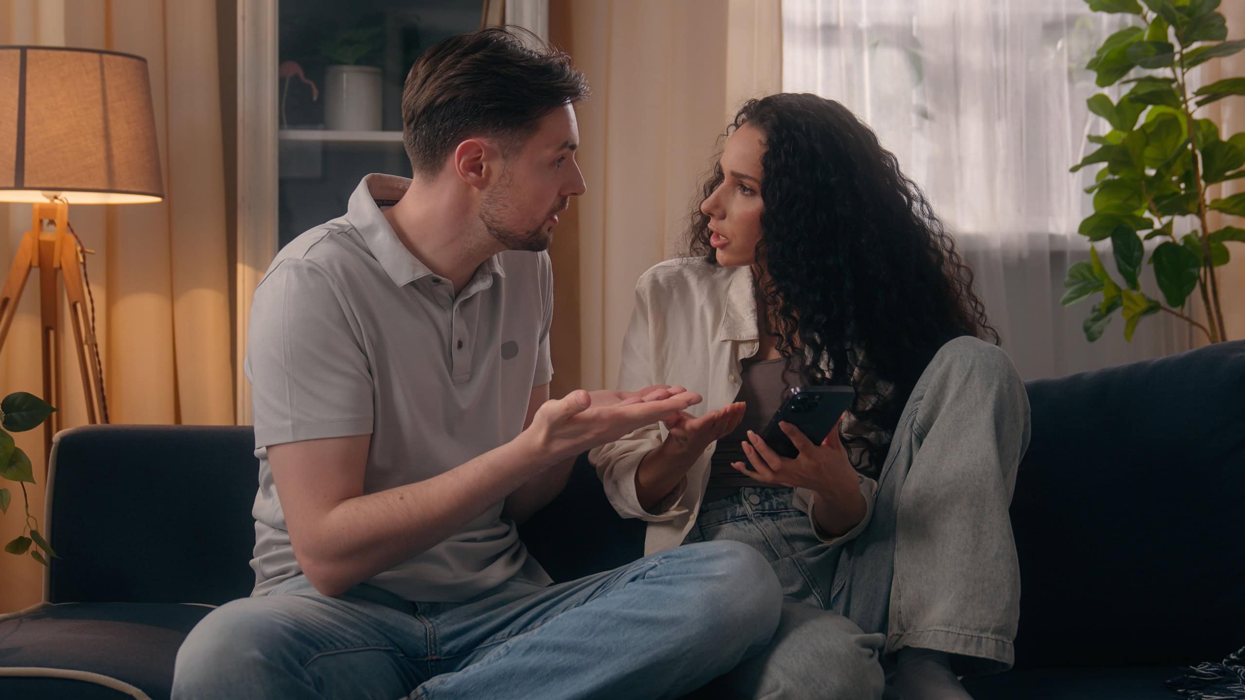 Caucasian couple problem conflict discuss social media misunderstanding quarrel man male husband boyfriend with Hispanic woman female girl girlfriend wife holding home mobile phone online arguing