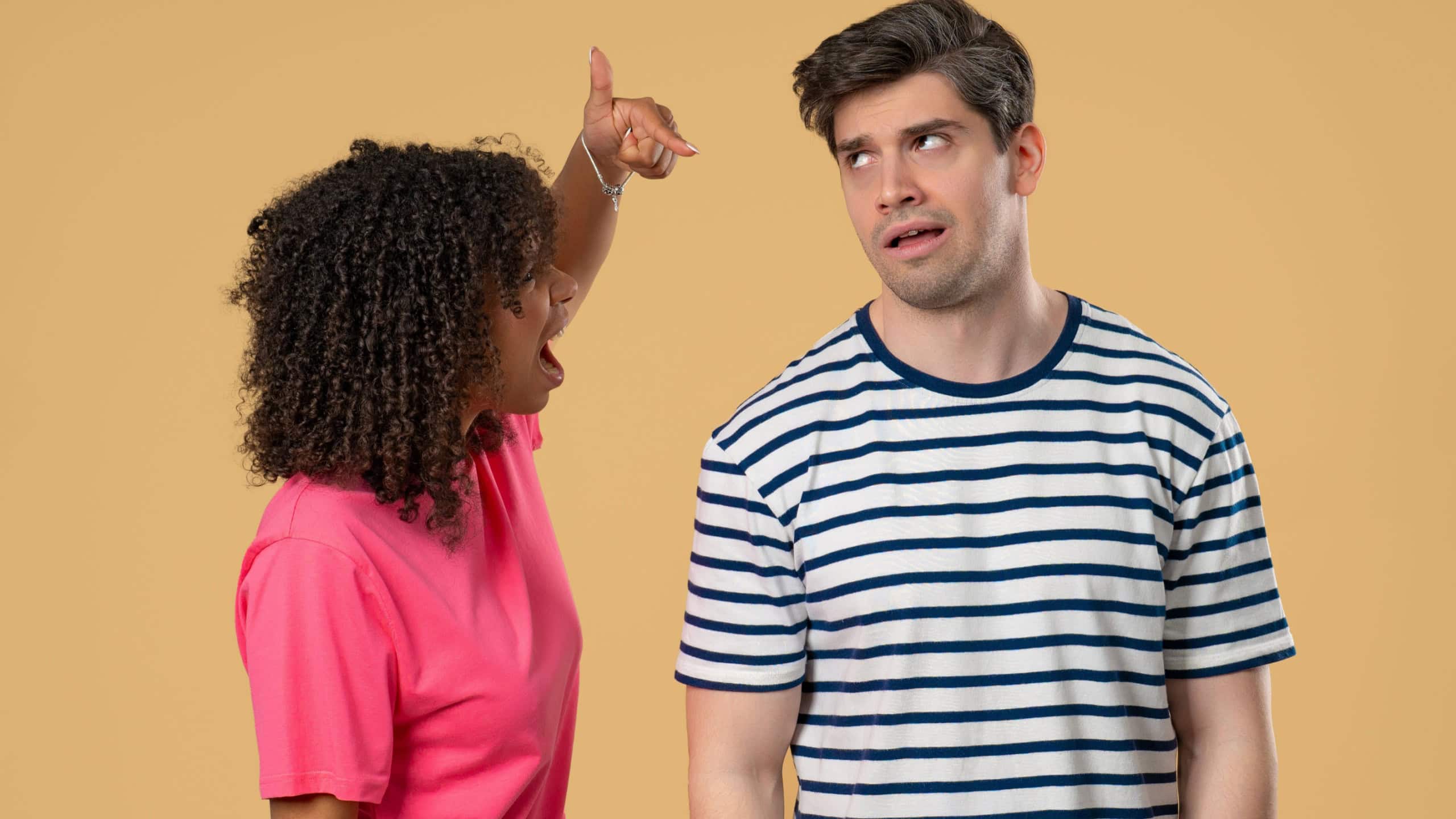 Young african american woman scolds boyfriend or husband On beige solid wall background. Tired man rolling eyes. Concept of conflict, quarrel, problems in Interracial couple relationships.High quality