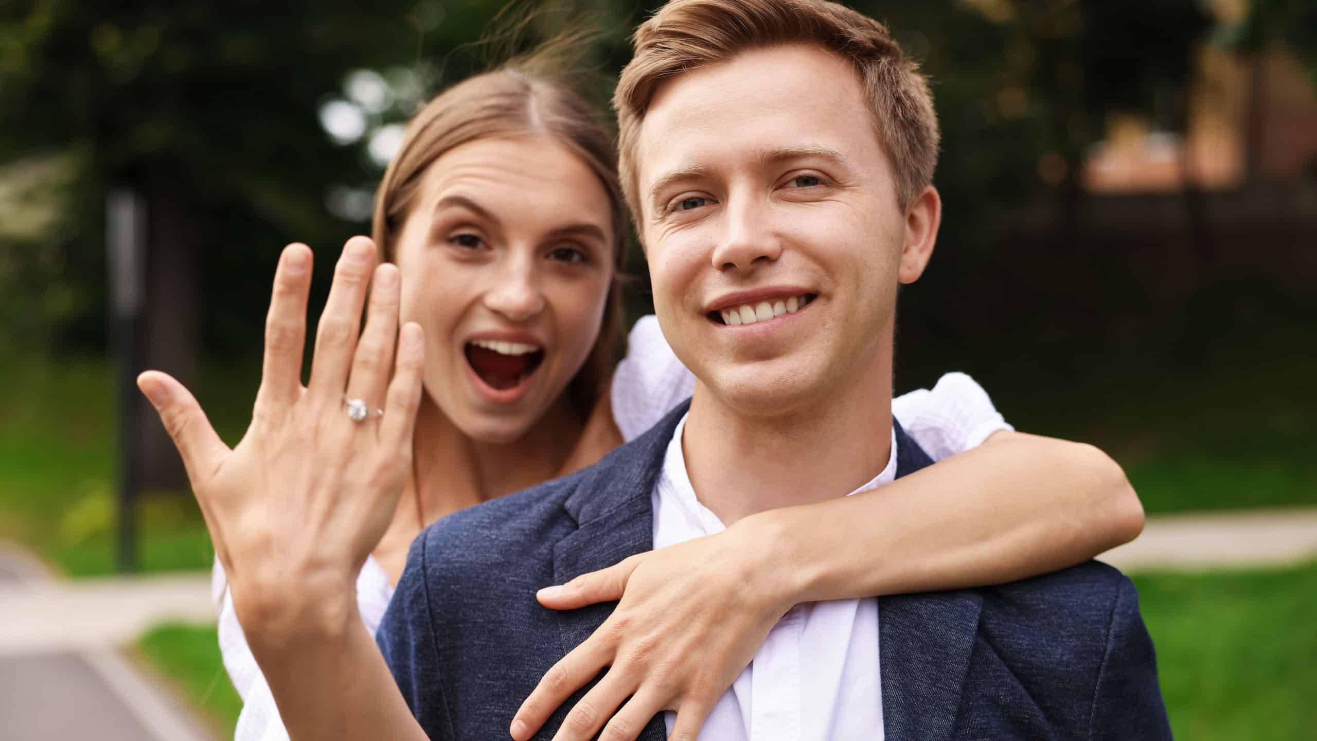 Marriage proposal. Excited woman showing engagement ring and hugging her fiance outdoors