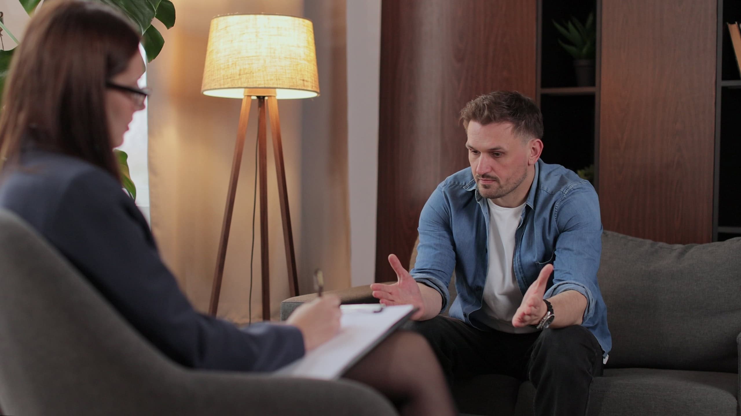 Therapy counselor patient stress anxiety support depression session. A worried man leans forward as the psychologist takes notes, offering help in office. Mental health and psychology.