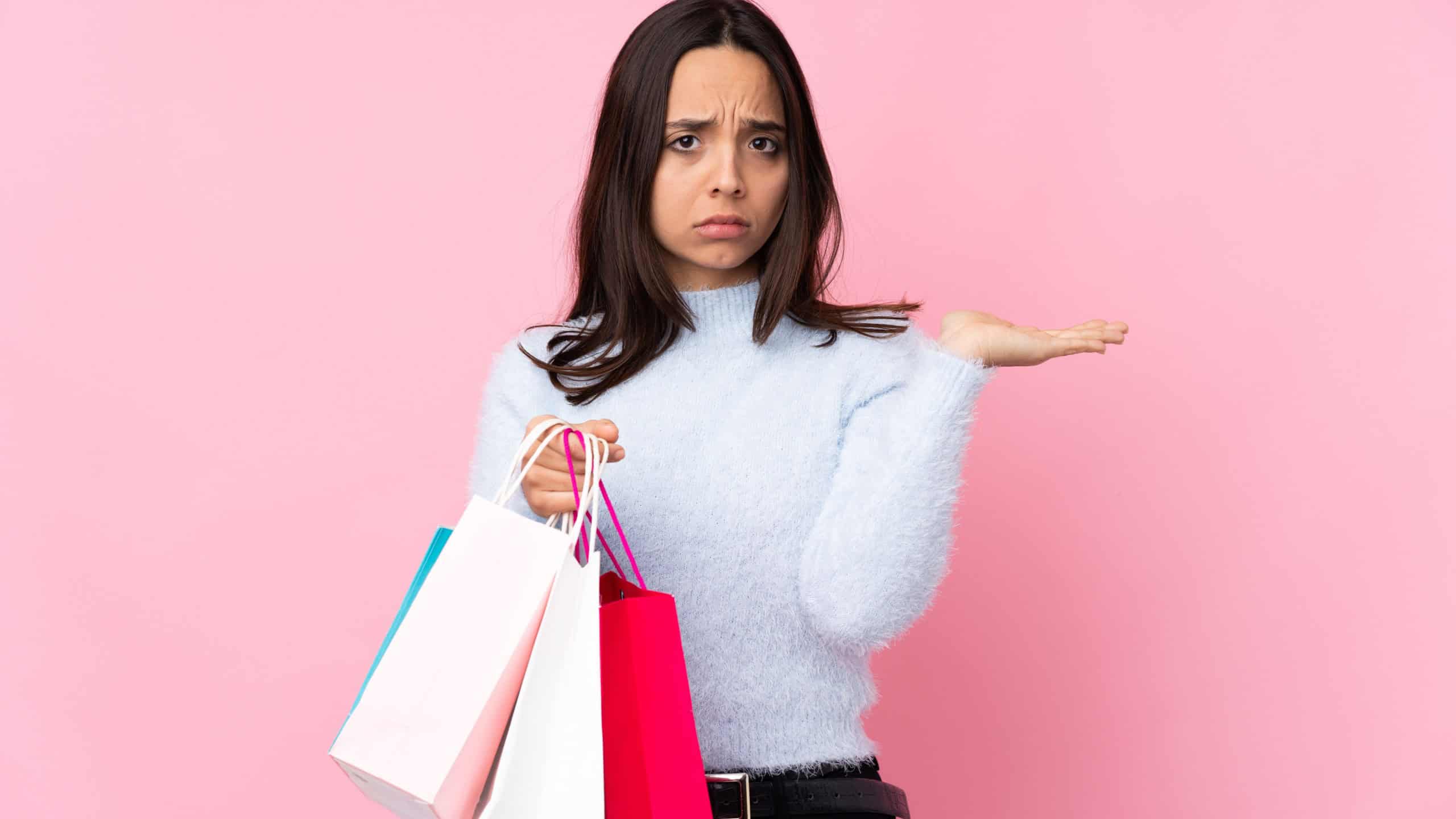 Young woman with shopping bag over isolated pink background unhappy for not understand something