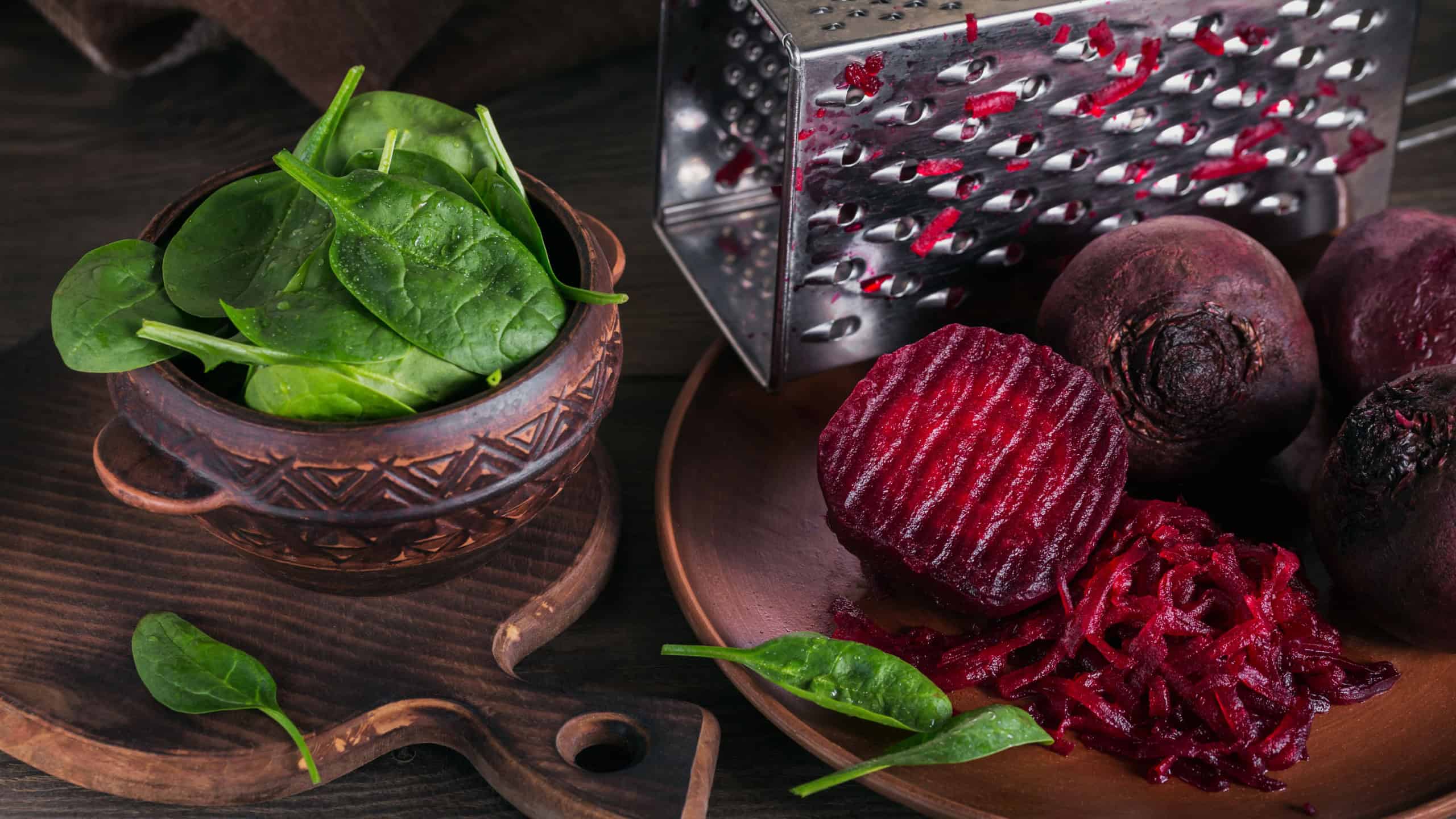 Prepearing beetroot salad on dark wooden background. Cooked beets and baby spinach leaves in clay bowl