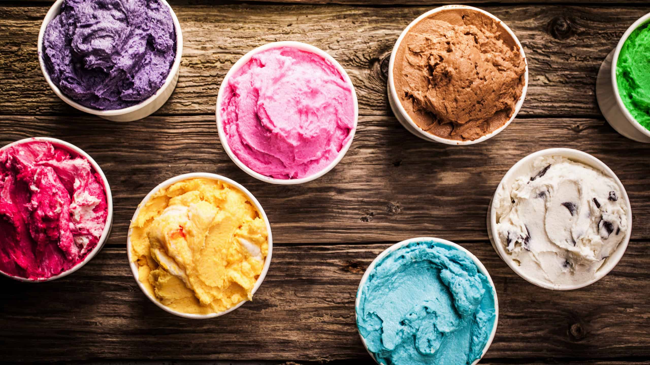 Selection of gourmet flavours of Italian ice cream in vibrant colors served in individual plastic tubs on an old rustic wooden table in an ice cream parlor, overhead view