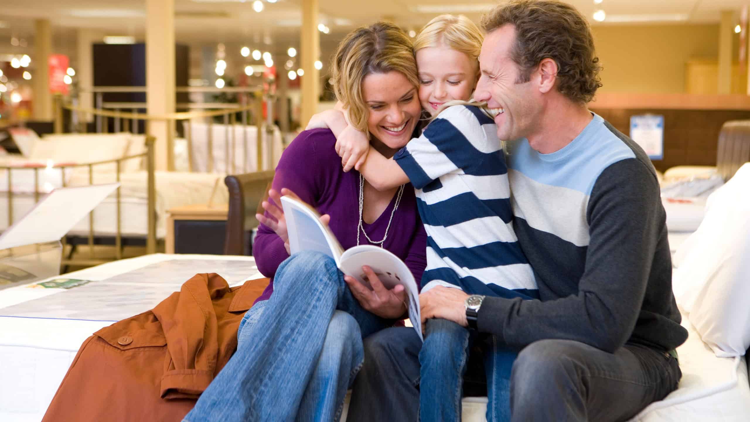 Little girl hugging her mother while her parents are sitting and checking out a catalog