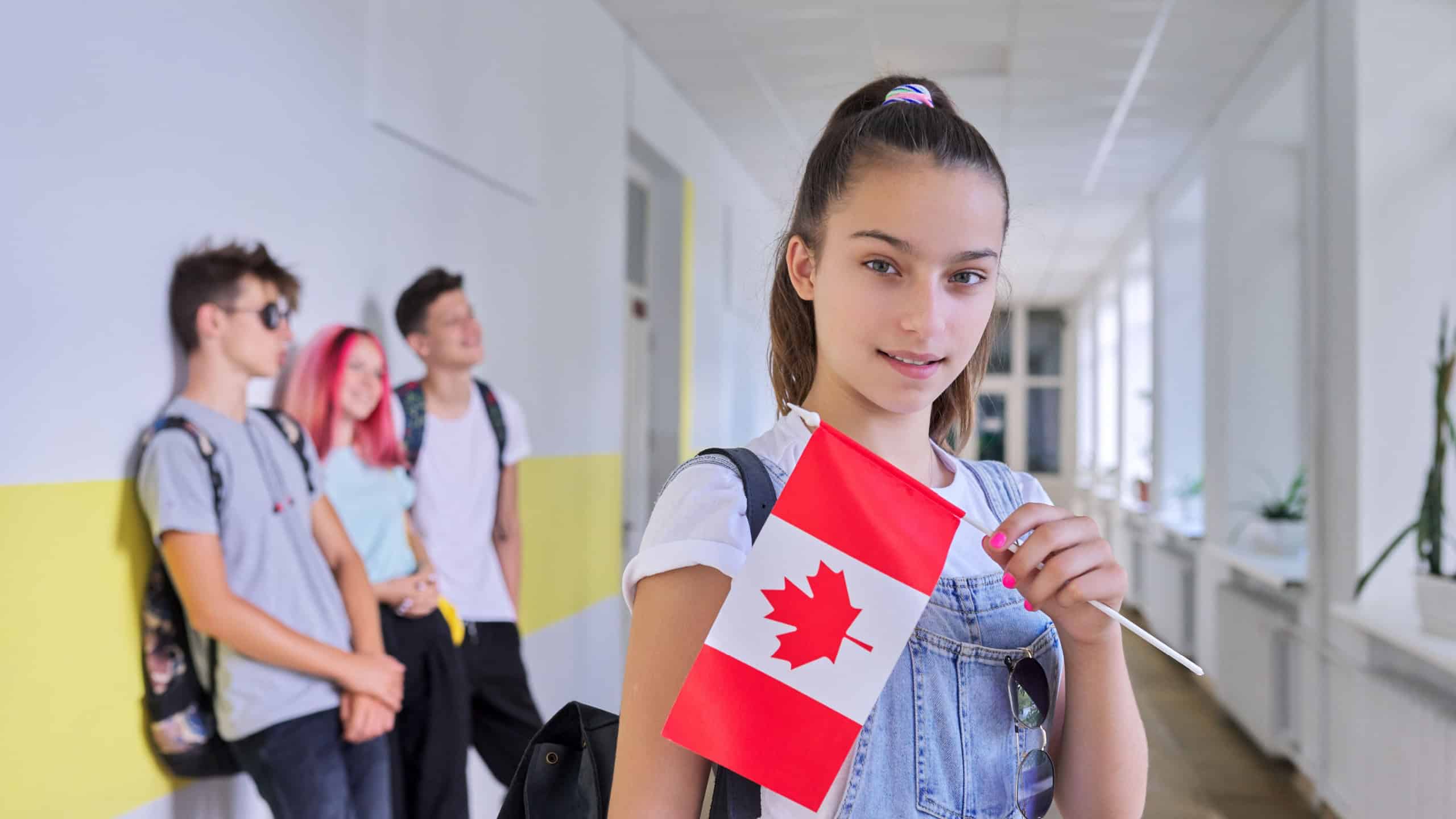 Student teenager female with flag of Canada inside school, children group background. Canada, education and youth, patriotism, people concept