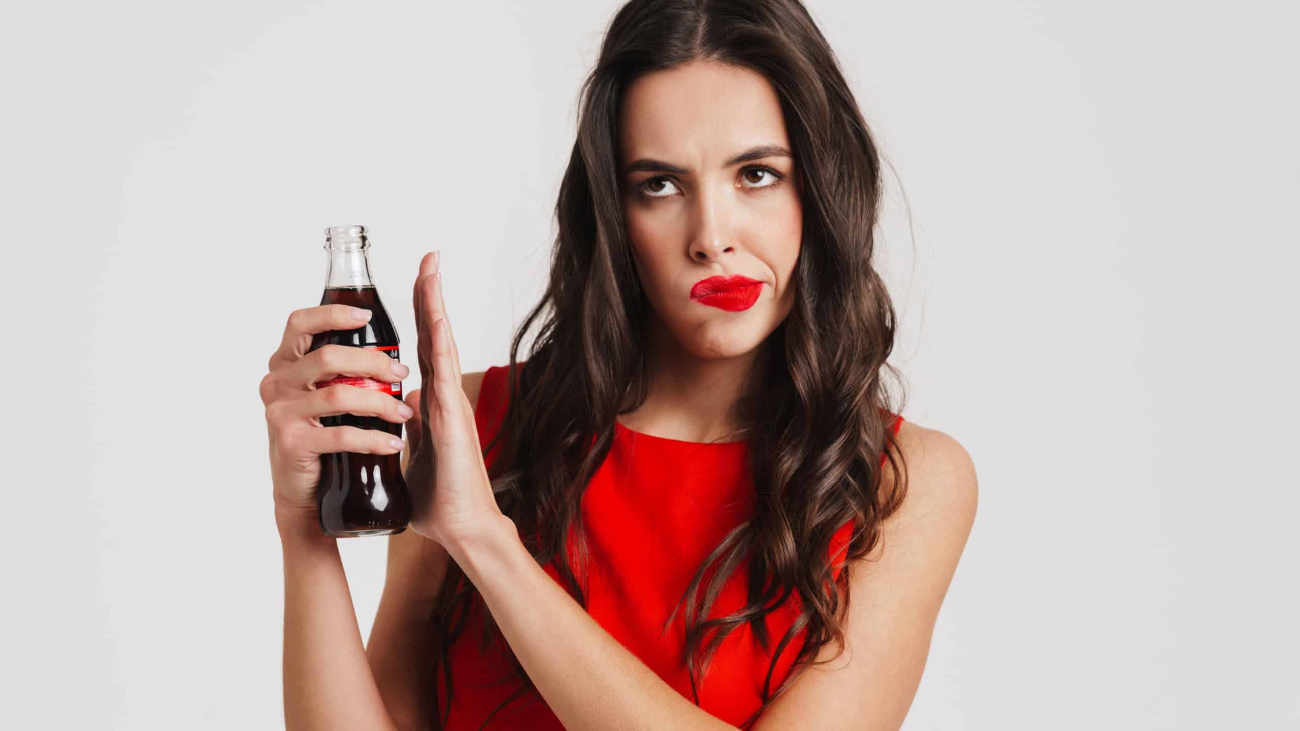 Young upset beautiful woman refuses to drink sweet fizzy drink isolated over gray background