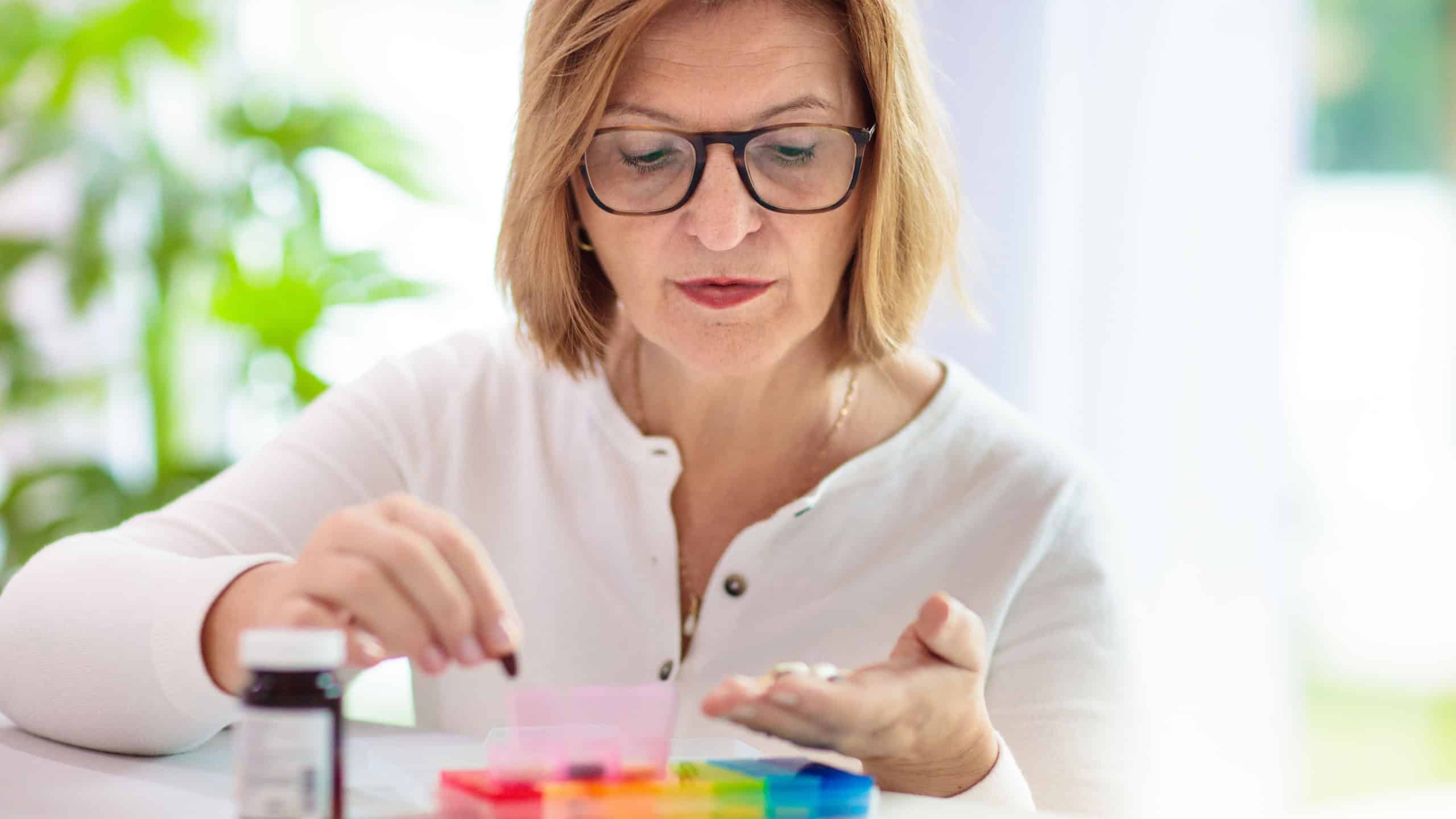 Pill box for senior patient. Medicine container. Elderly woman sorting drug pills for pain relief and disease treatment. Sick retired female with drugs. Daily vitamins for healthy retirement.
