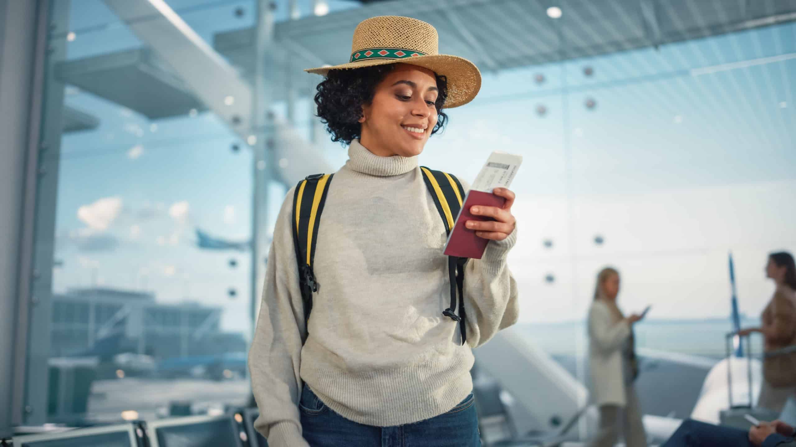 Airport Terminal: Happy Traveling Black Woman Looks Around Searching Flight Gates and Plane, Uses Smartphone, Checking Trip Destination on Internet. African American Female Wondering on Vacation