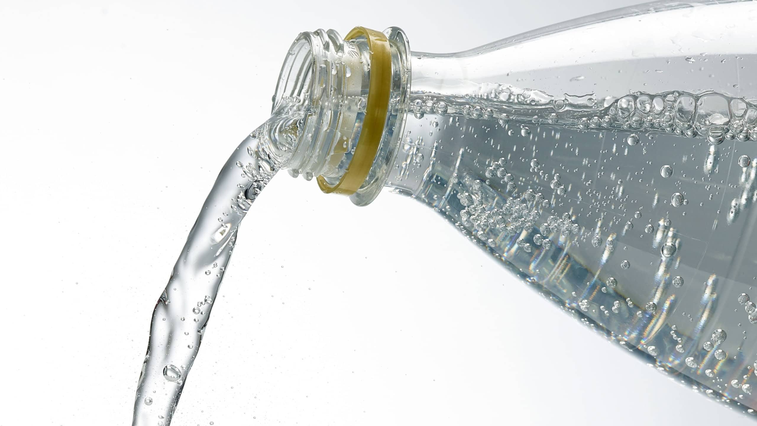 Sparkling water pouring from plastic bottle on white background