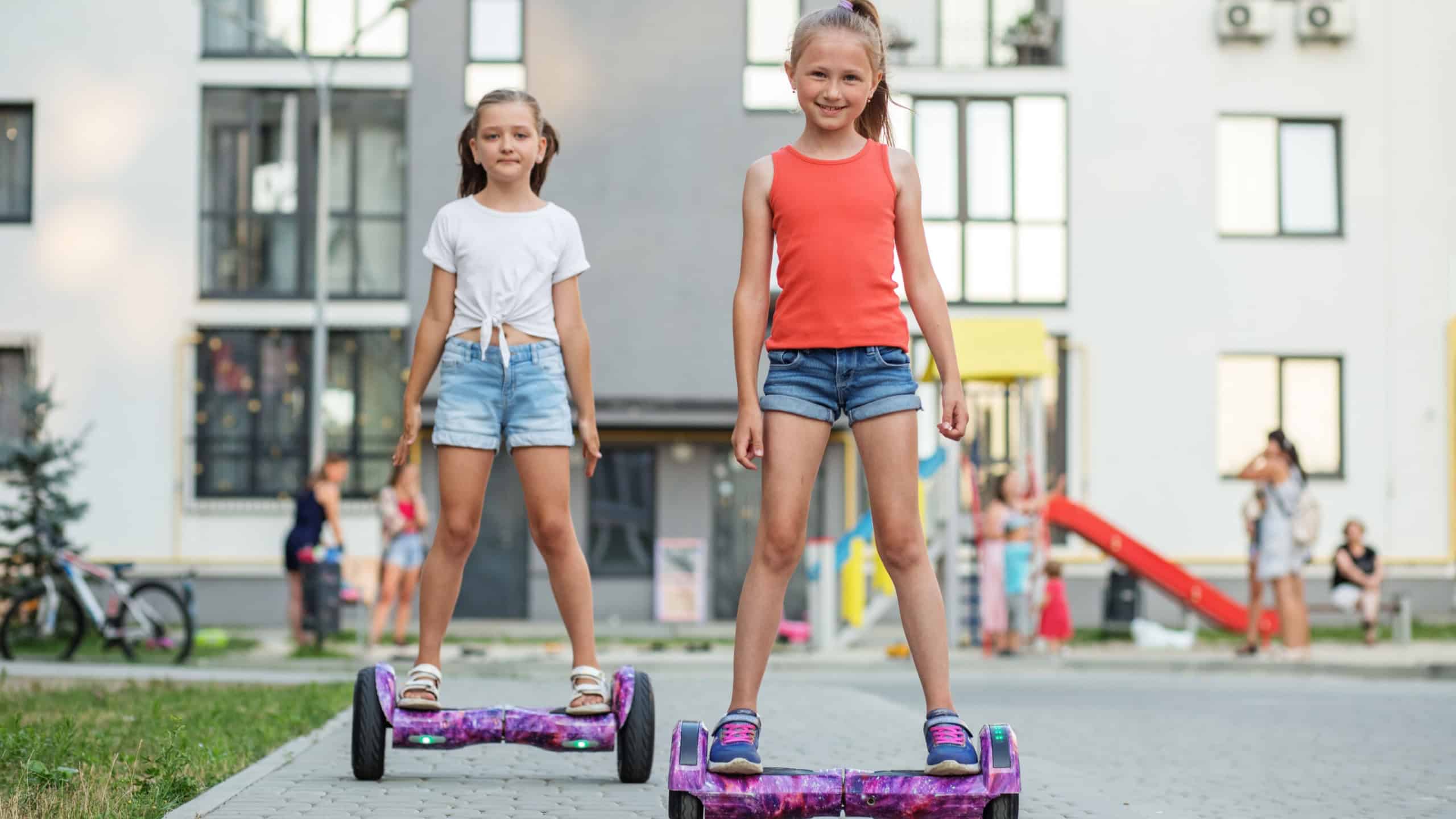 Active life concept. Happy children riding on hoverboards or gyro scooters outdoors in summer. Playground near multi-storey building.