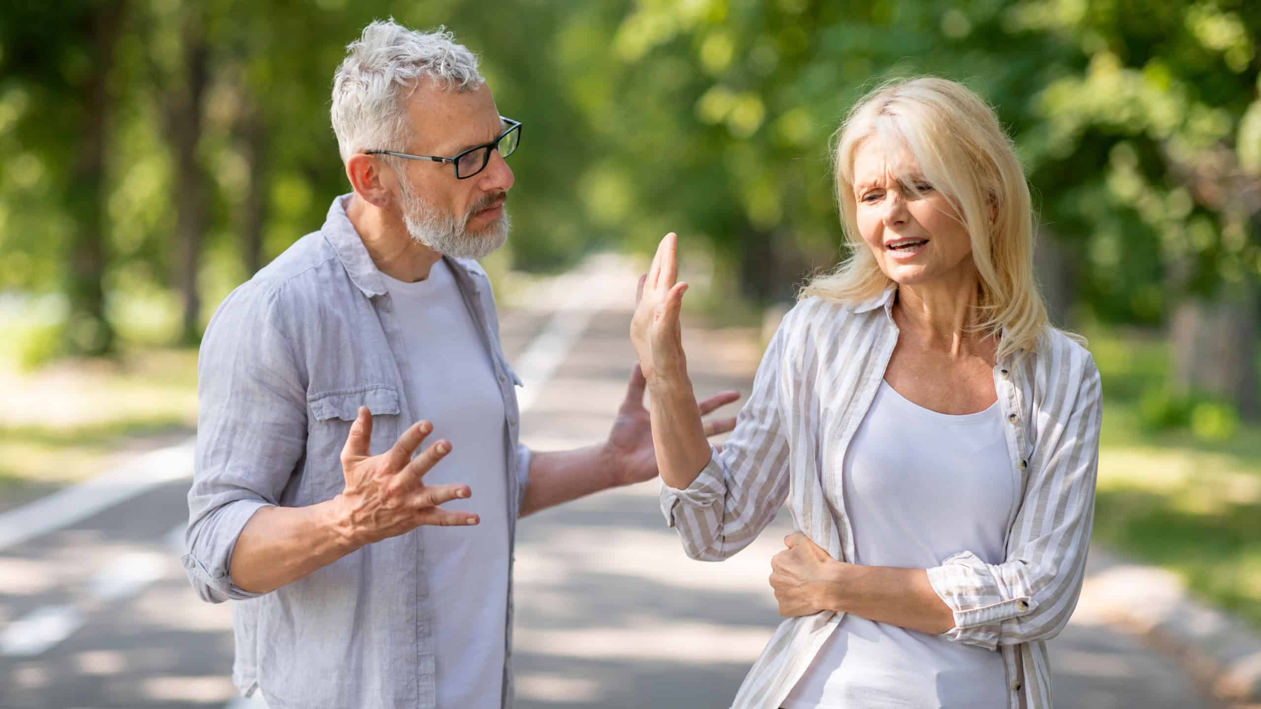 Older Couple Conflicts. Mature Spouses Arguing While Walking In Park, Angry Senior Man And Woman Quarreling Outdoors, Suffering Misunderstanding And Marital Crisis, Wife Making Stop Gesture With Hand