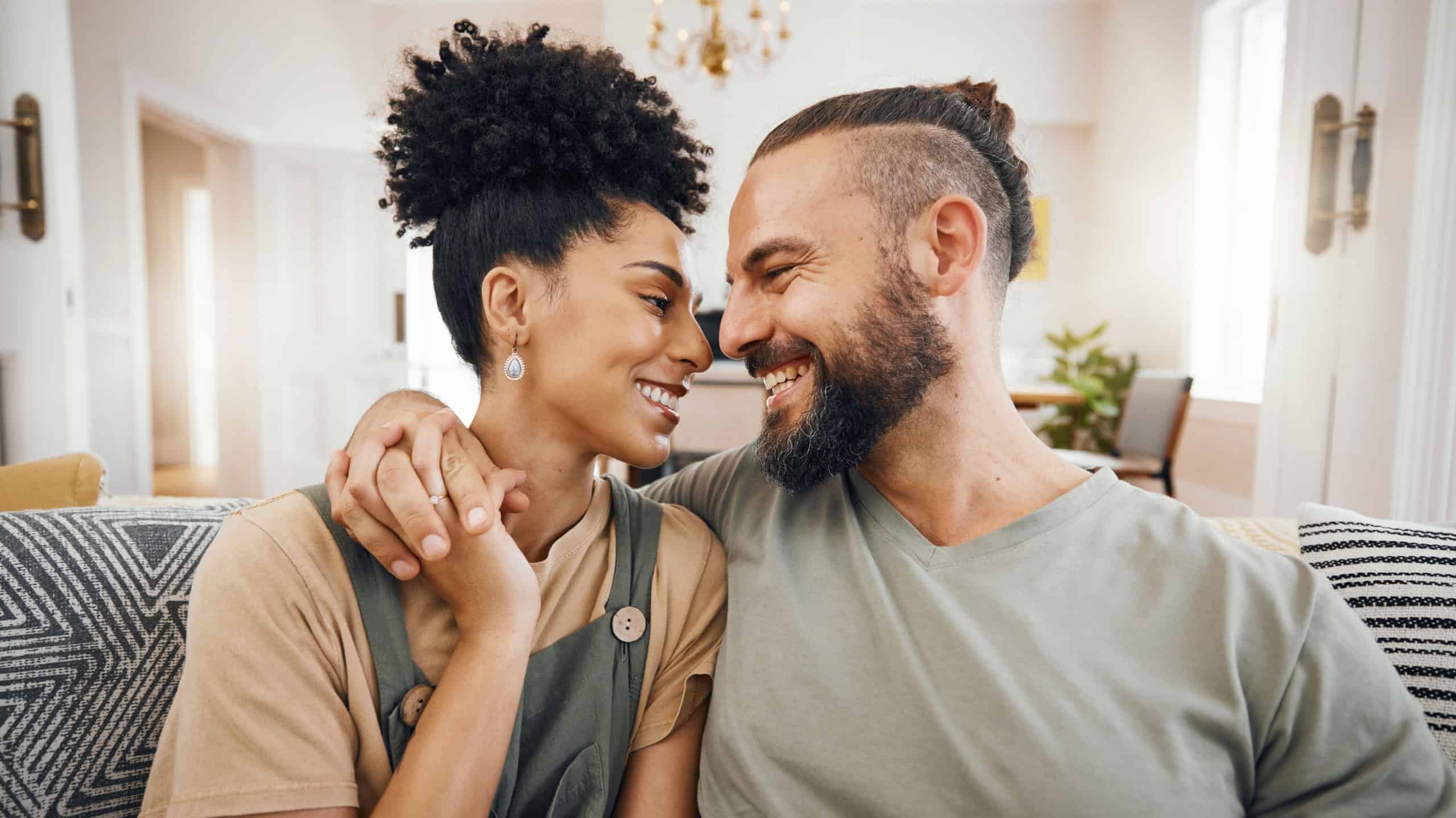 Happy, love or interracial couple on a sofa, care or commitment with relationship, weekend break or loving together. Home, man or woman on a couch, marriage or romantic with bonding, date or relax