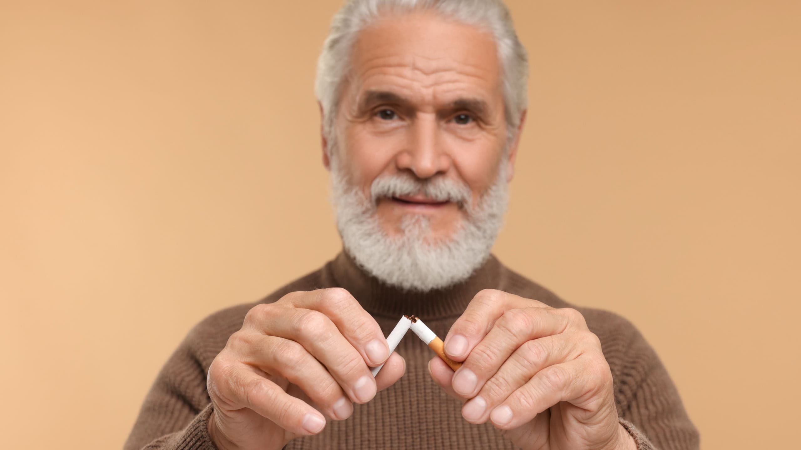 Stop smoking concept. Senior man breaking cigarette on beige background, selective focus