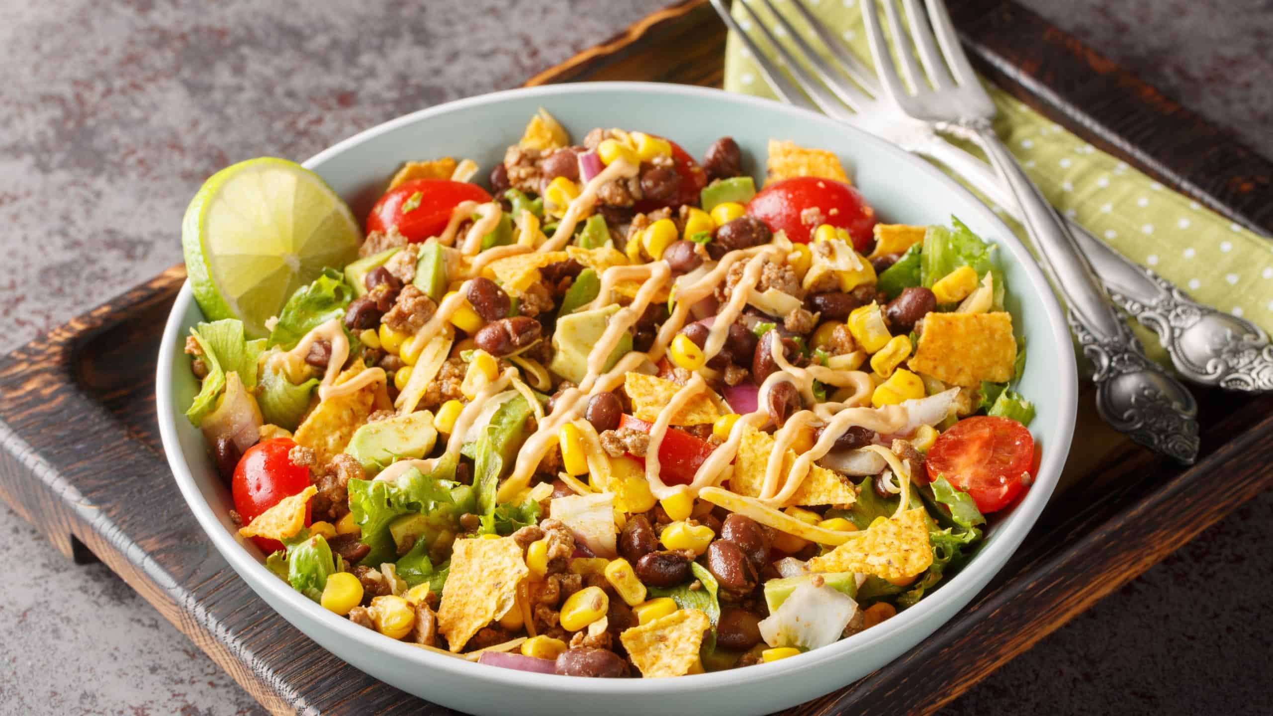 Ground beef taco salad with nacho chips, vegetable salsa, cheese dressed with cream sauce close-up on a plate on the table.