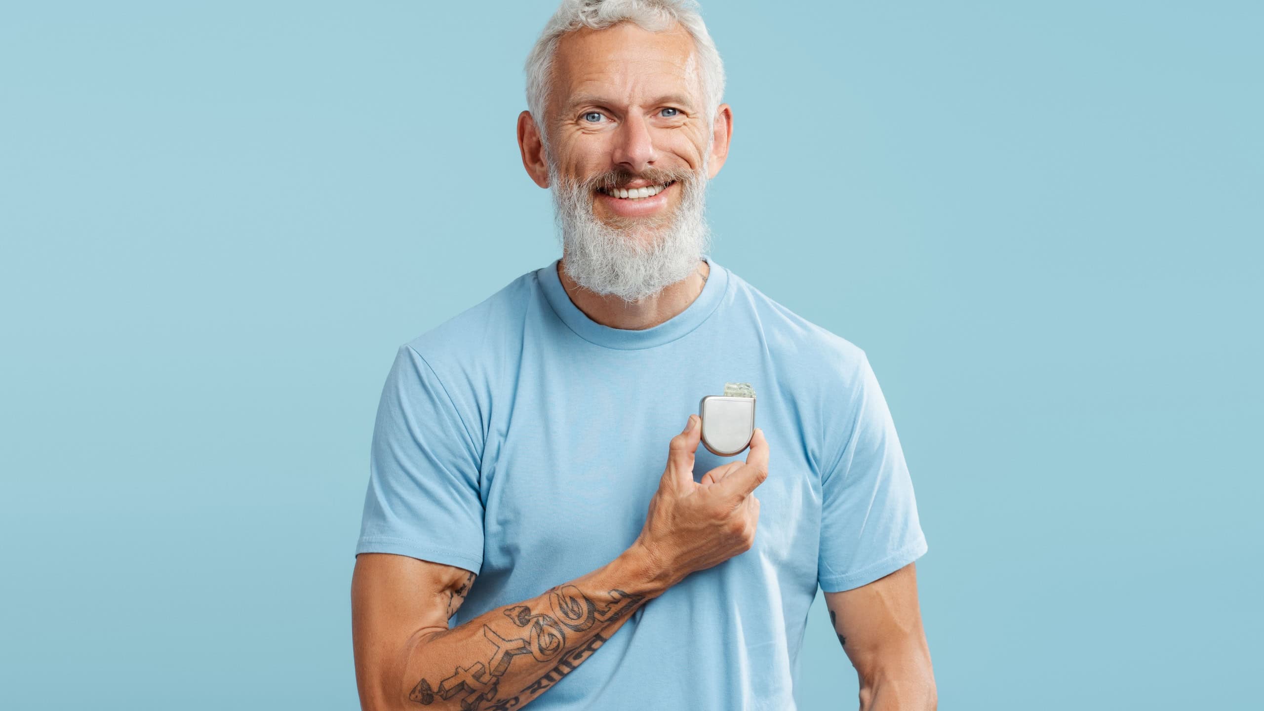 Portrait of attractive mature man in blue t shirt holding pacemaker in hands, looking at camera isolated on blue background. Health care, treatment concept