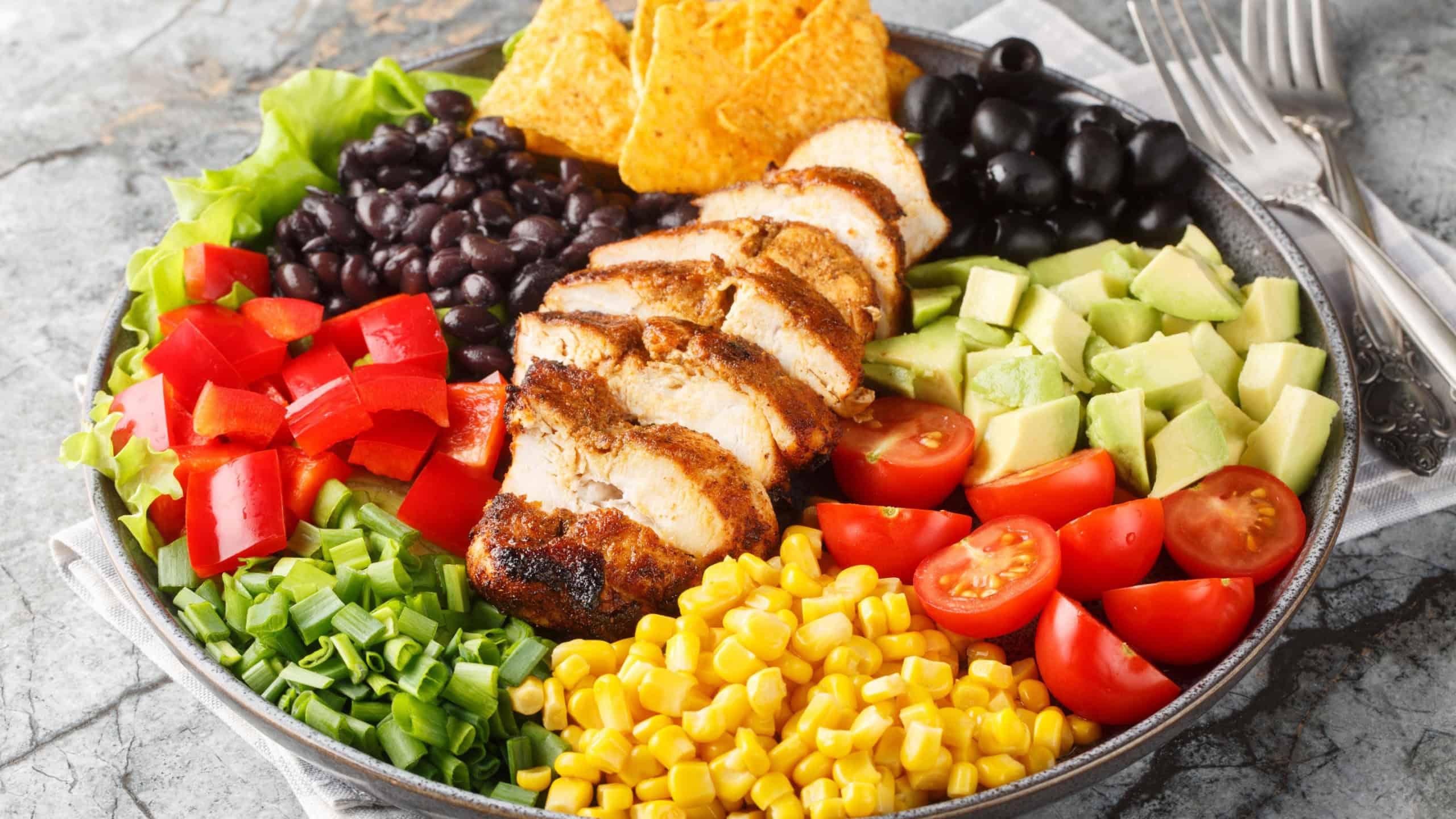 Tex-Mex Santa Fe chicken salad with lettuce, tomatoes, corn, black beans, pepper, avocado, olive closeup on the plate on the table. 