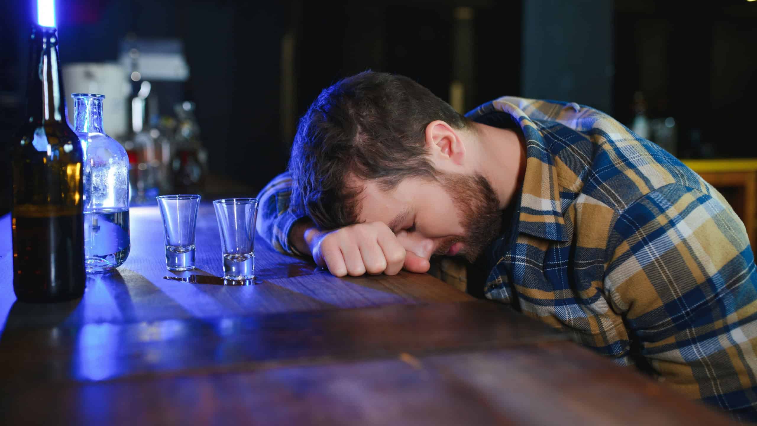 Drunk man sleeps at bar counter, alcohol addiction.