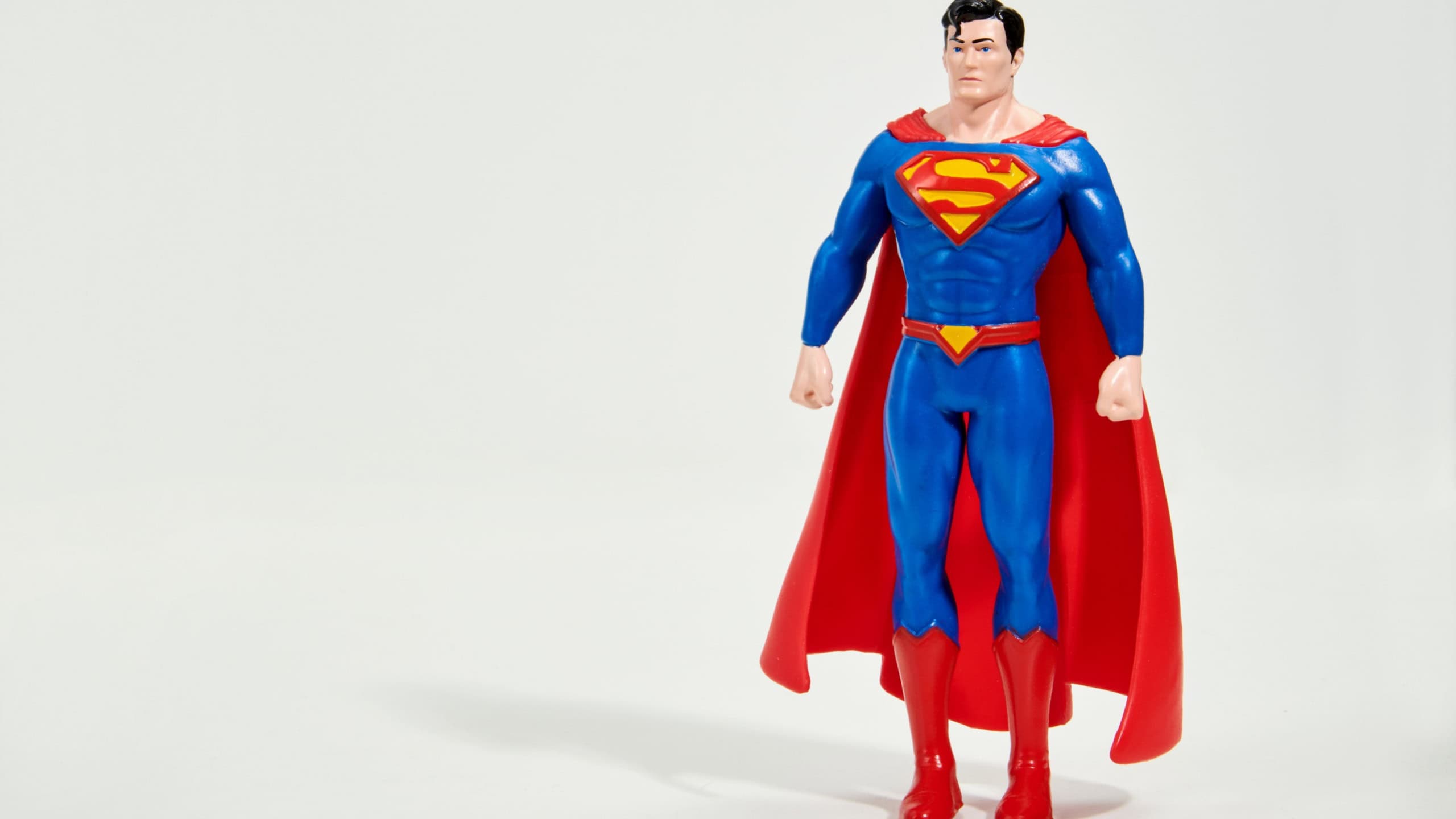 Figurine of Superman in classic blue costume with red cloak standing on white surface in studio