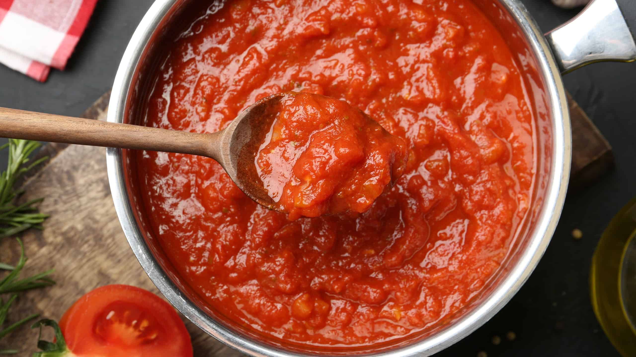 Homemade tomato sauce and spoon in pot on dark table, flat lay