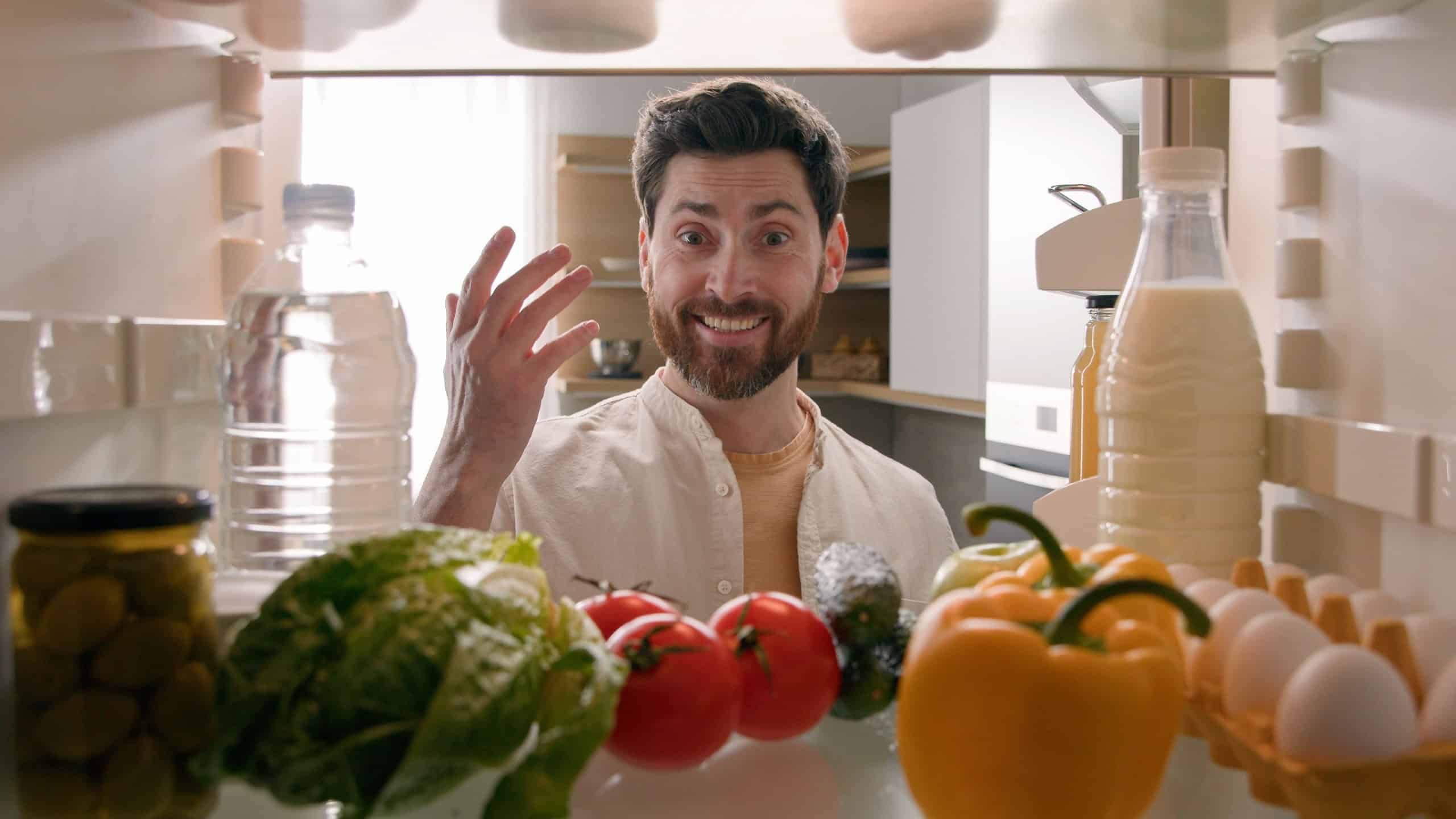 Point of view from inside refrigerator POV Caucasian man householder homeowner open fridge door kitchen full of products food smiling find take red tomato happy smile cooking salad healthy vegetarian