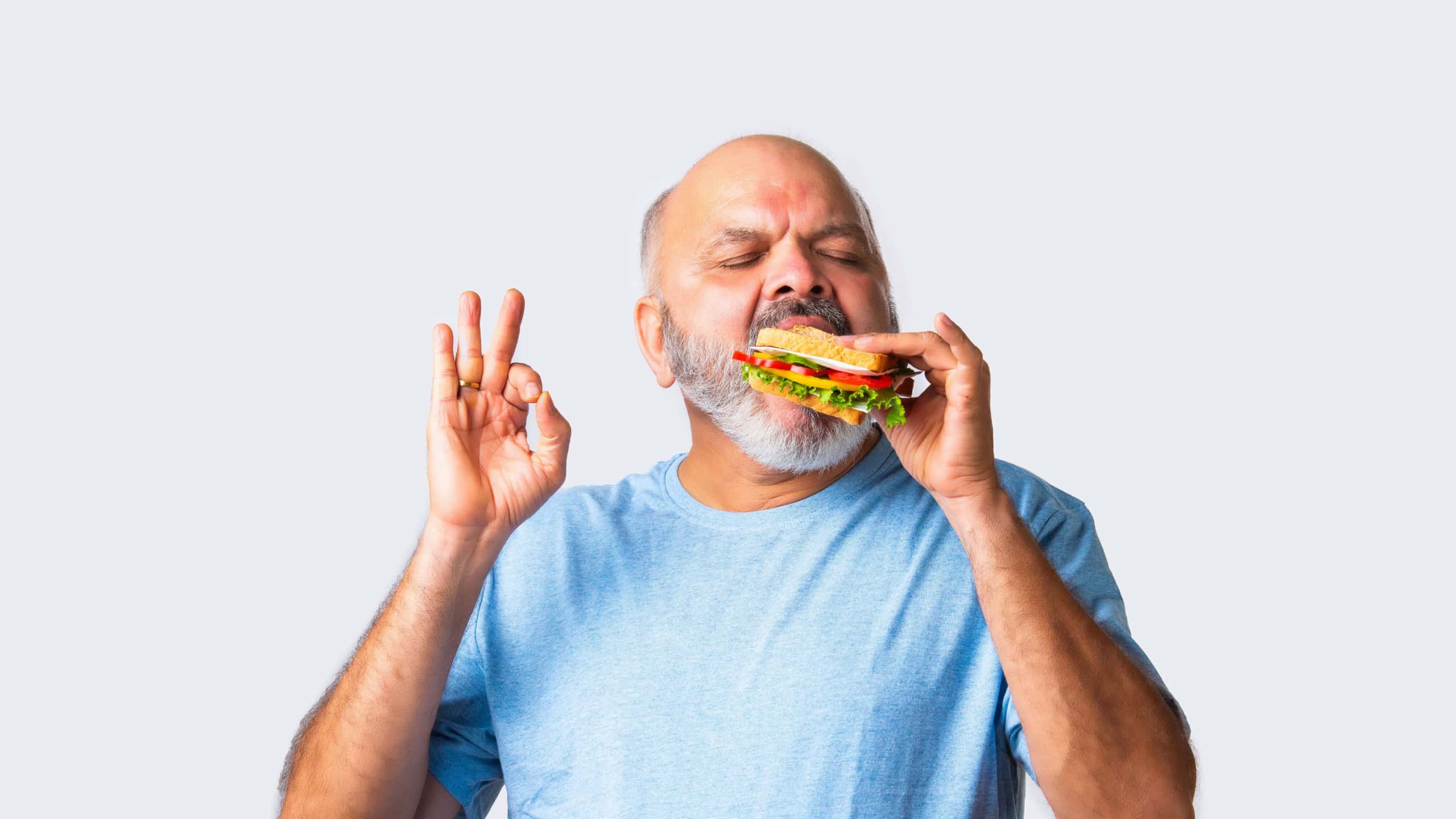 Asian Indian elderly old senior man eating tasty vegetable sandwich, isolated