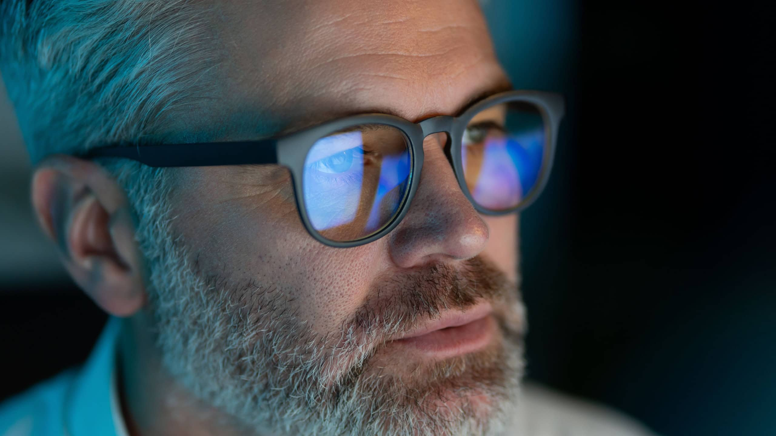 Close-Up Of Mature Man With Glasses Focused On Computer Screen, Reflections In Lenses, Dim Lighting, Late Night Work, Technology And Concentration