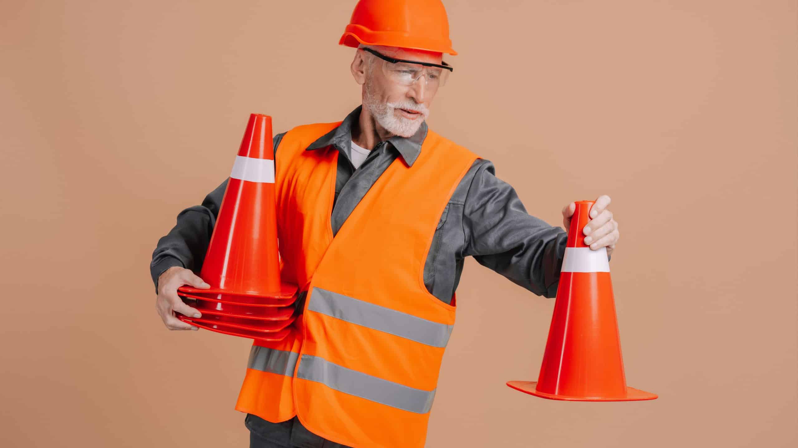 Experienced construction worker wearing a safety vest and hardhat is carefully positioning traffic cones, ensuring a secure work zone and preventing accidents