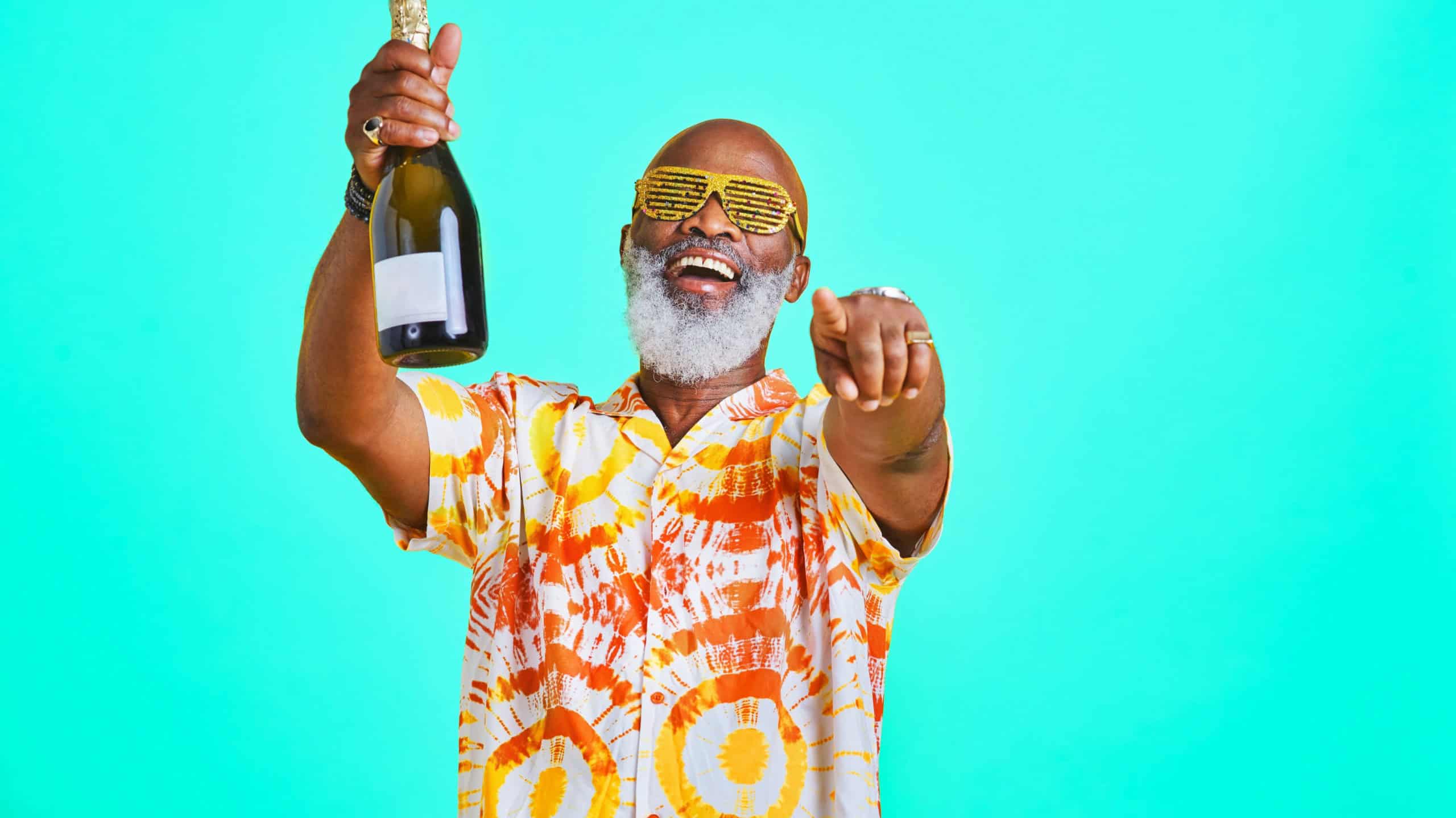 Mature man, champagne and celebration in studio for birthday party, happiness and festival even. Black person, alcohol and cool sunglasses for holiday, pointing or New Year concert on blue background