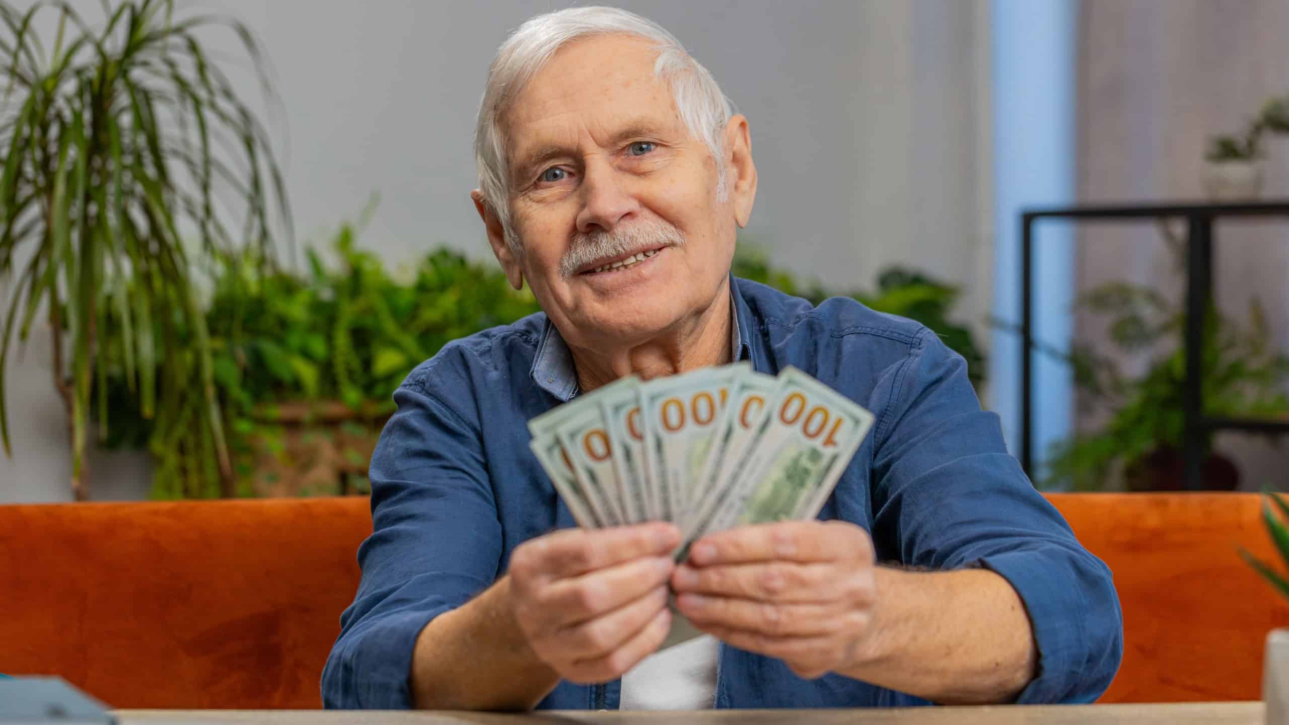 Planning family budget. Happy senior man counting money cash calculate domestic bills at home. Mature old grandfather satisfied of income salary pension and saves money for planned vacation gifts