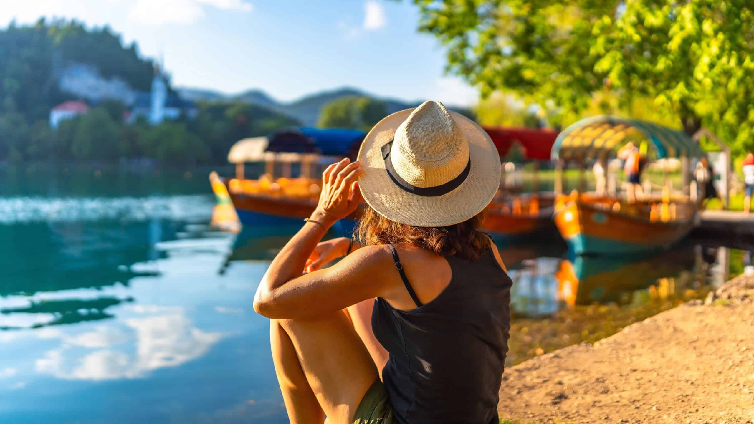 Woman enjoying summer vacation at lake bled, slovenia, with traditional pletna boats and bled island in the background