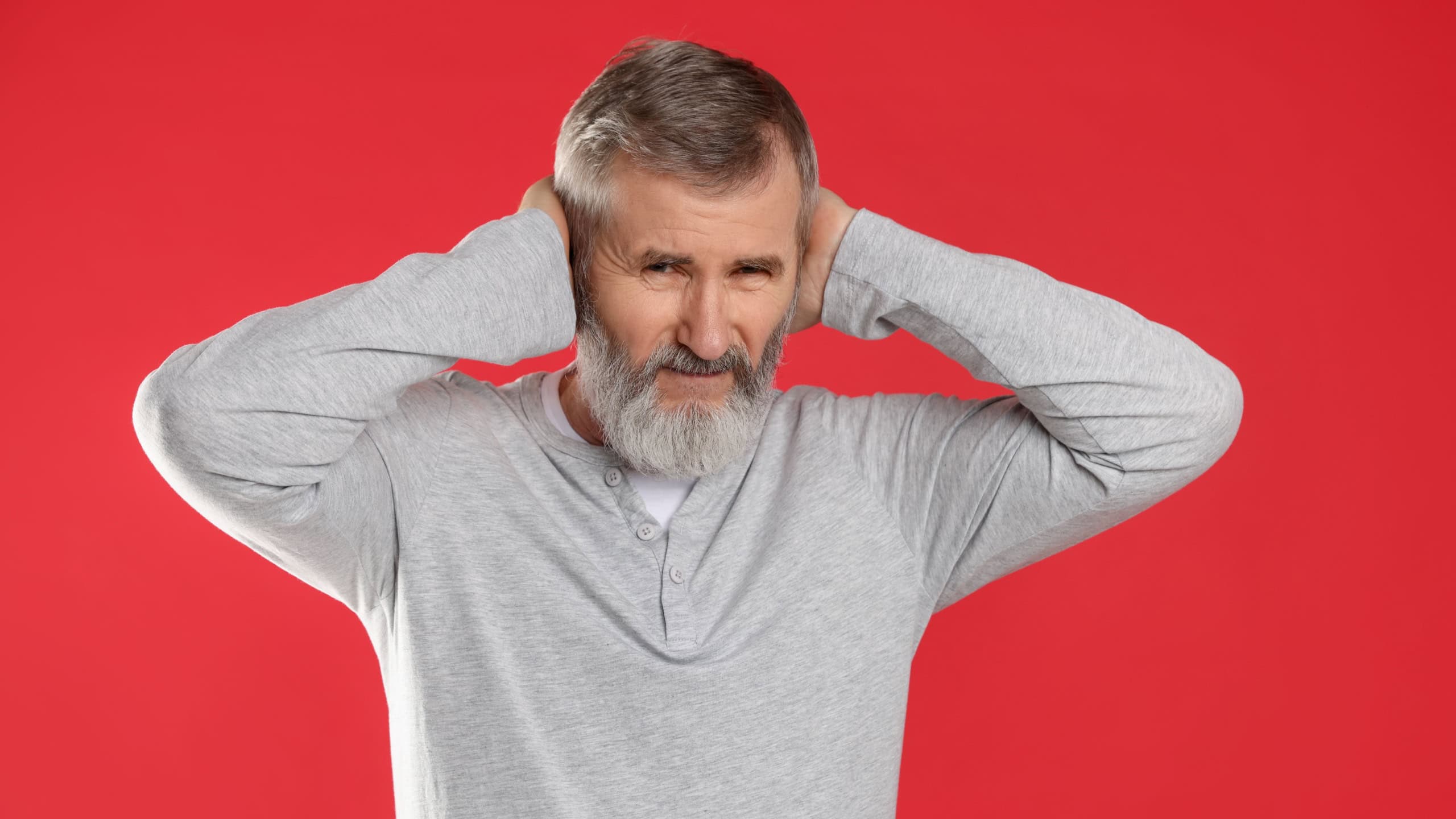 Senior man covering his ears on red background