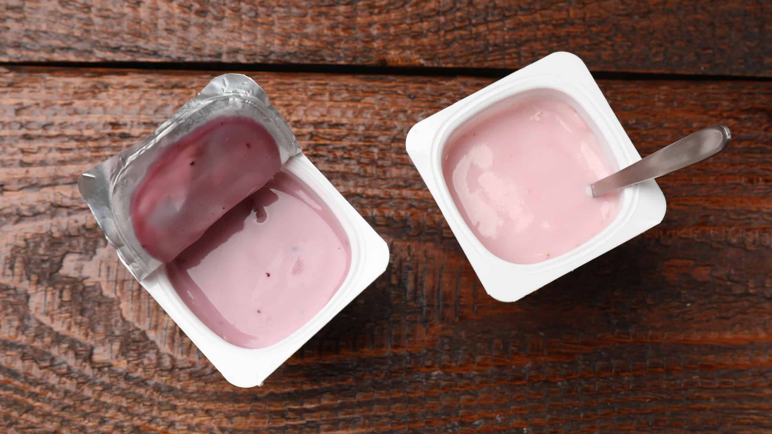 Delicious yogurts in plastic cups on wooden table, flat lay