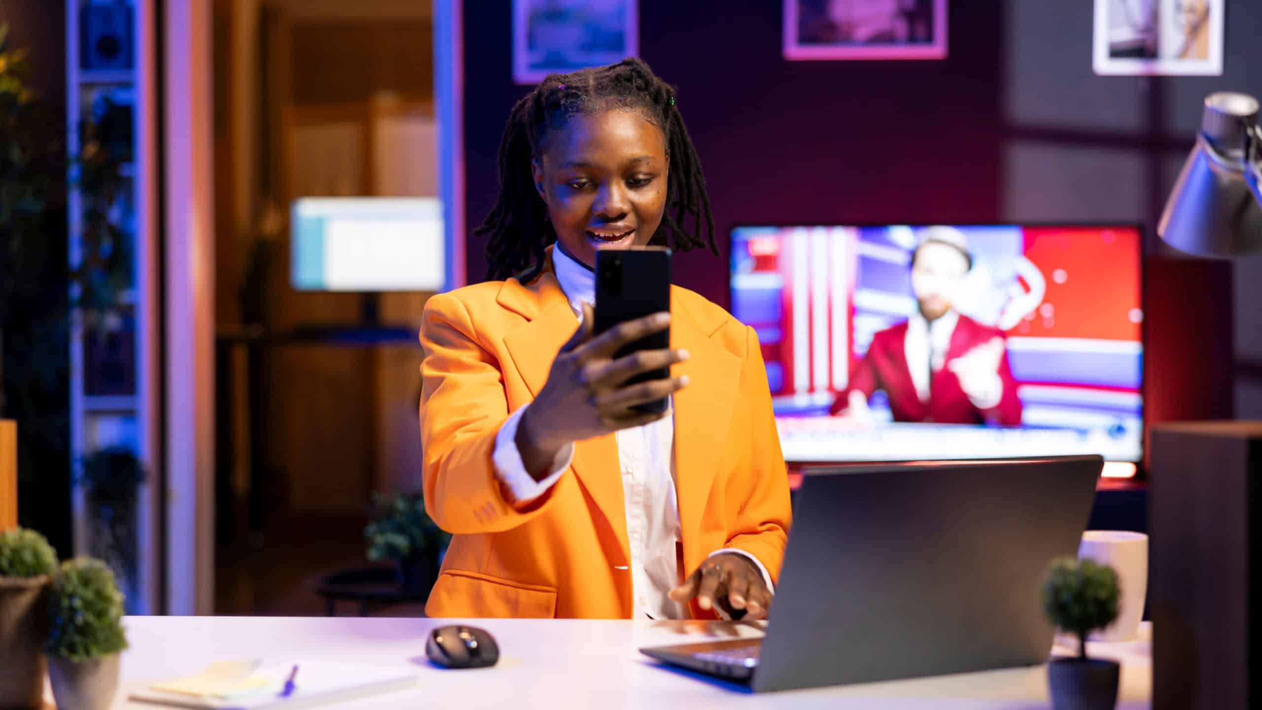 Smiling teenager in living room watching videos on social media using mobile phone. African american woman having fun looking at social network website content on smartphone
