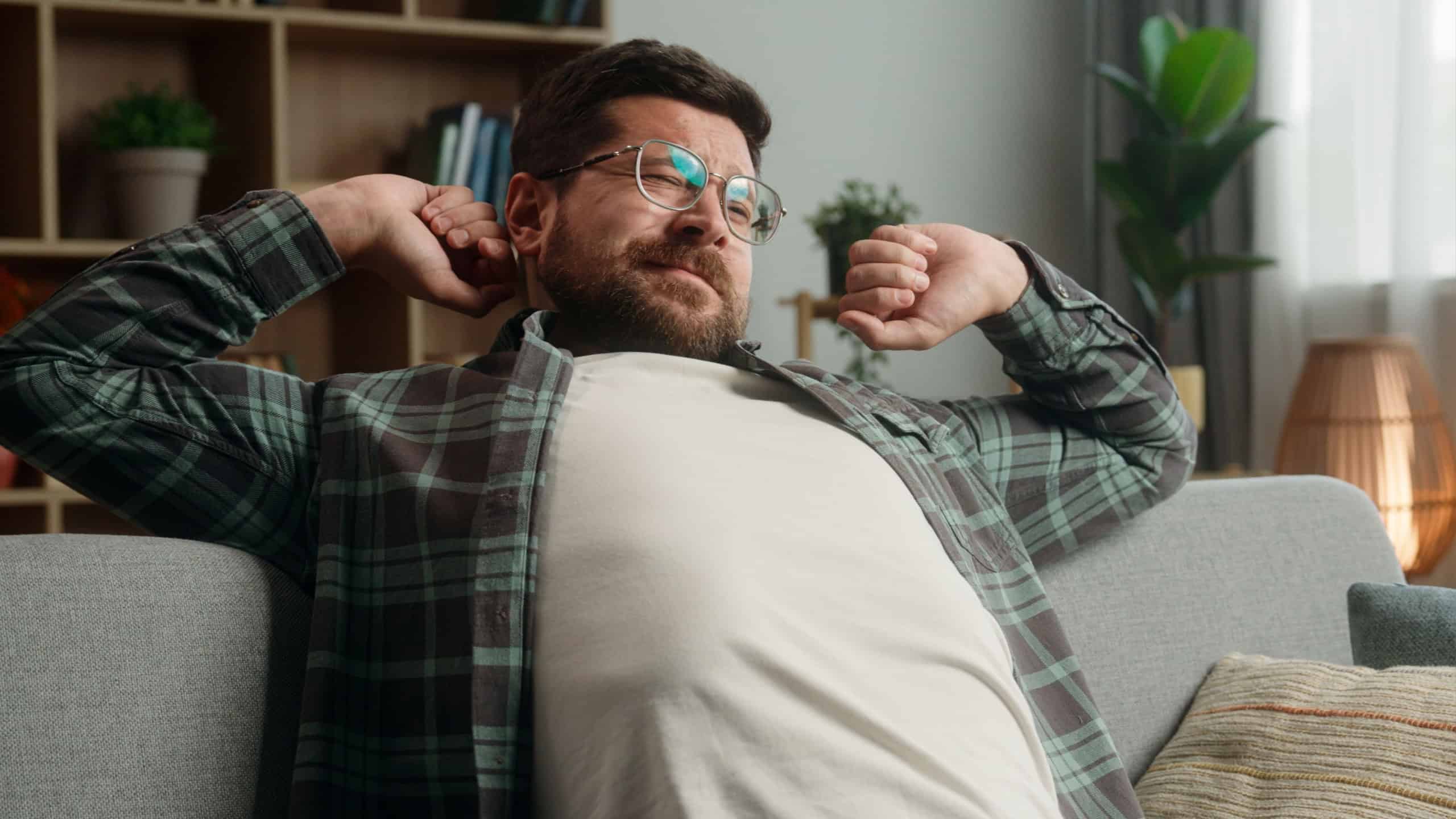 Smiling lazy relaxing resting Caucasian man guy male homeowner relax at couch sofa own rent home loan mortgage yawning stretching hands sleepy napping yawn sleep calm weekend indoors smile insomnia