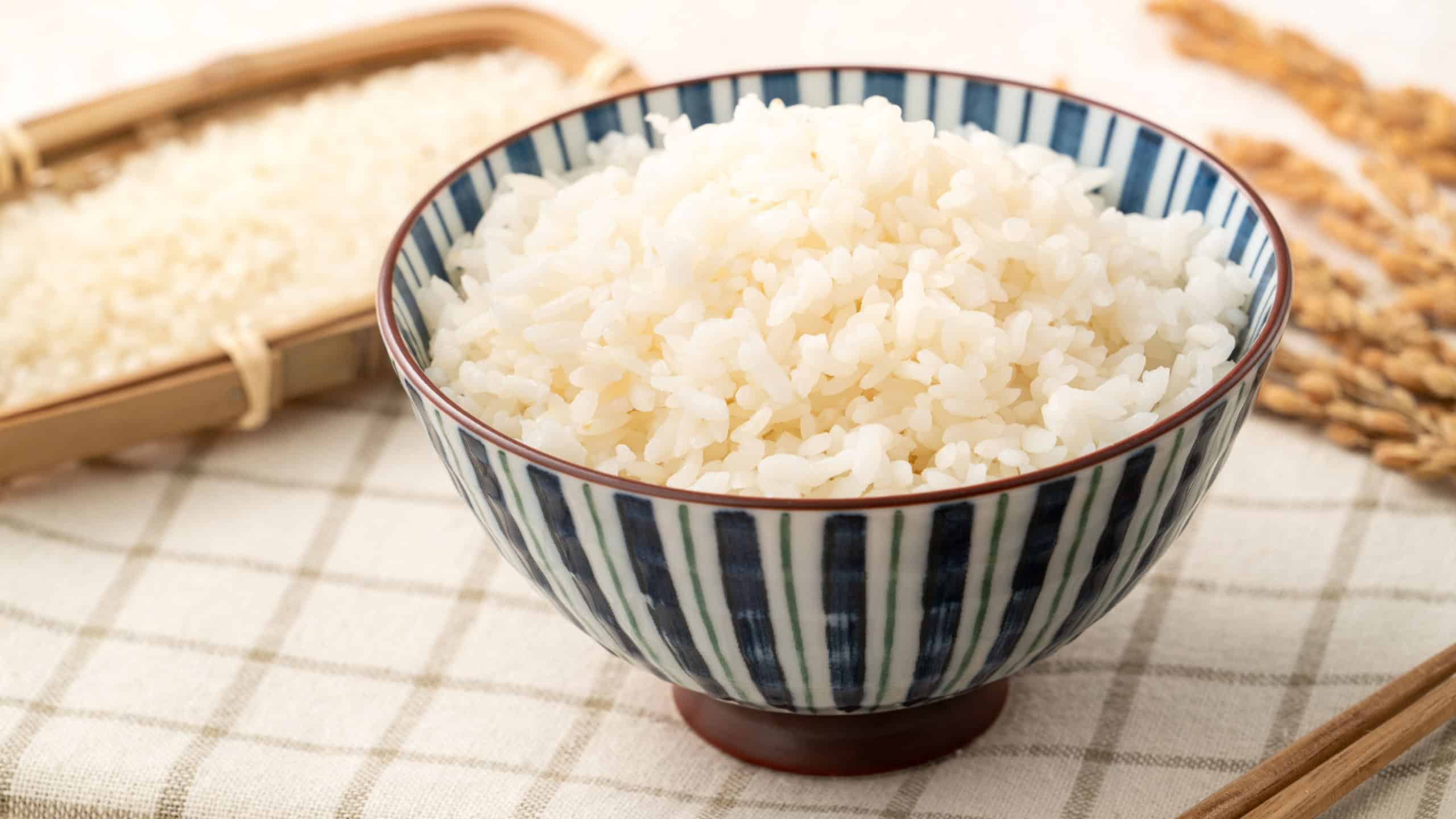 A bowl of freshly cookd steamed white rice, soft, fluffy, and slightly glossy on white table background.