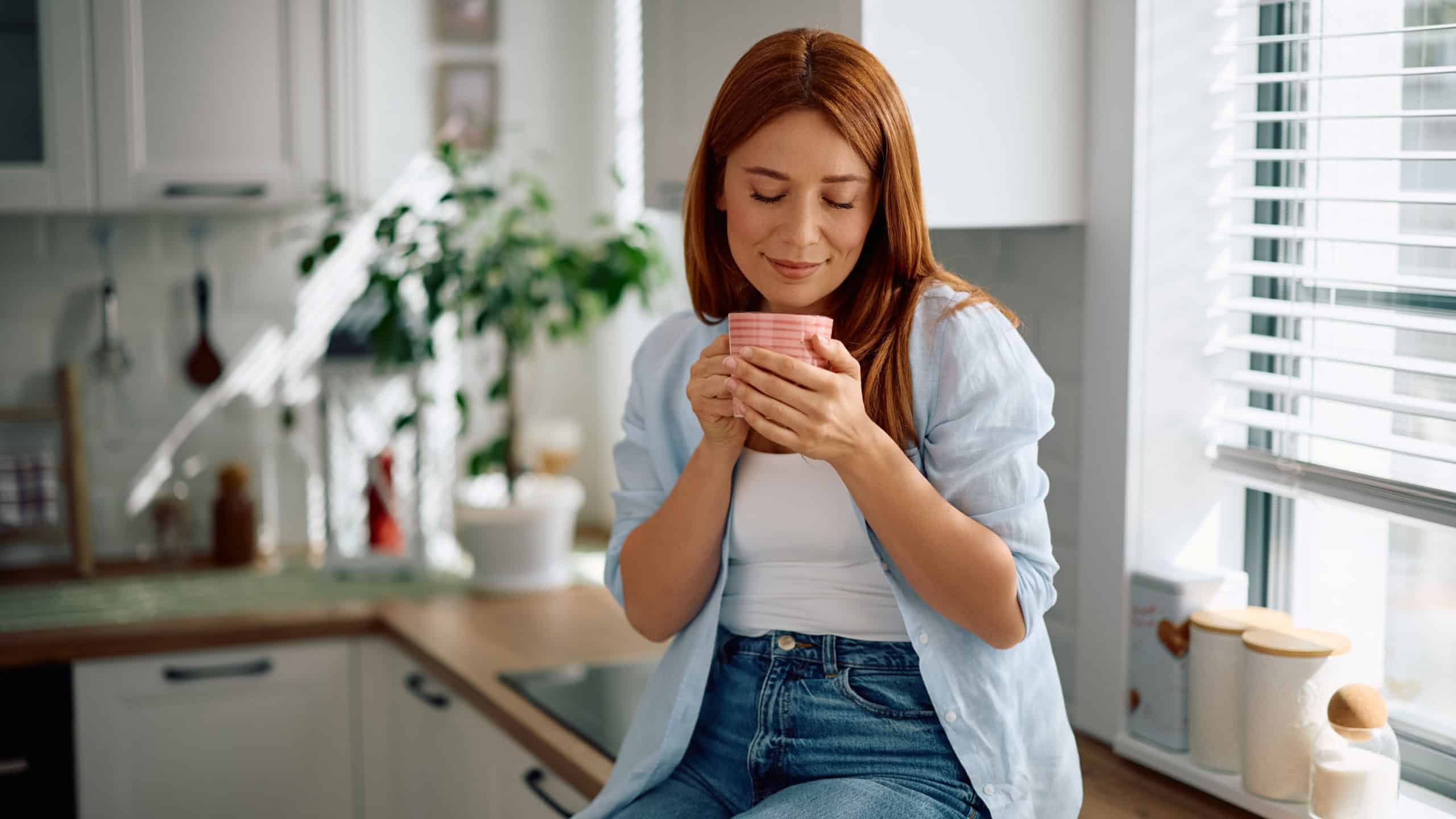 Woman with eyes closed enjoying in smell of morning coffee in the kitchen.